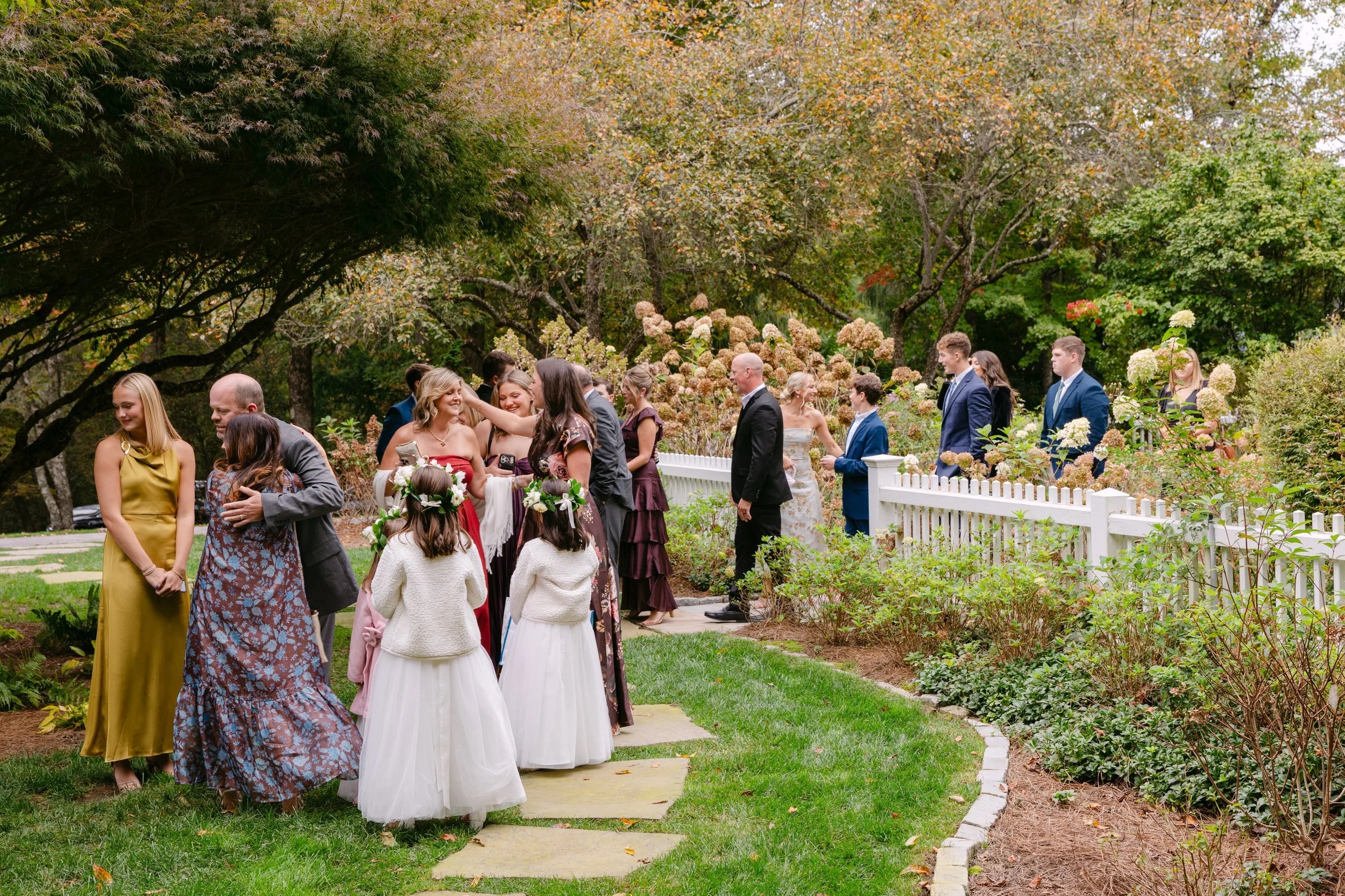 Wedding guests gathered in an autumn garden with hydrangeas and a white picket fence