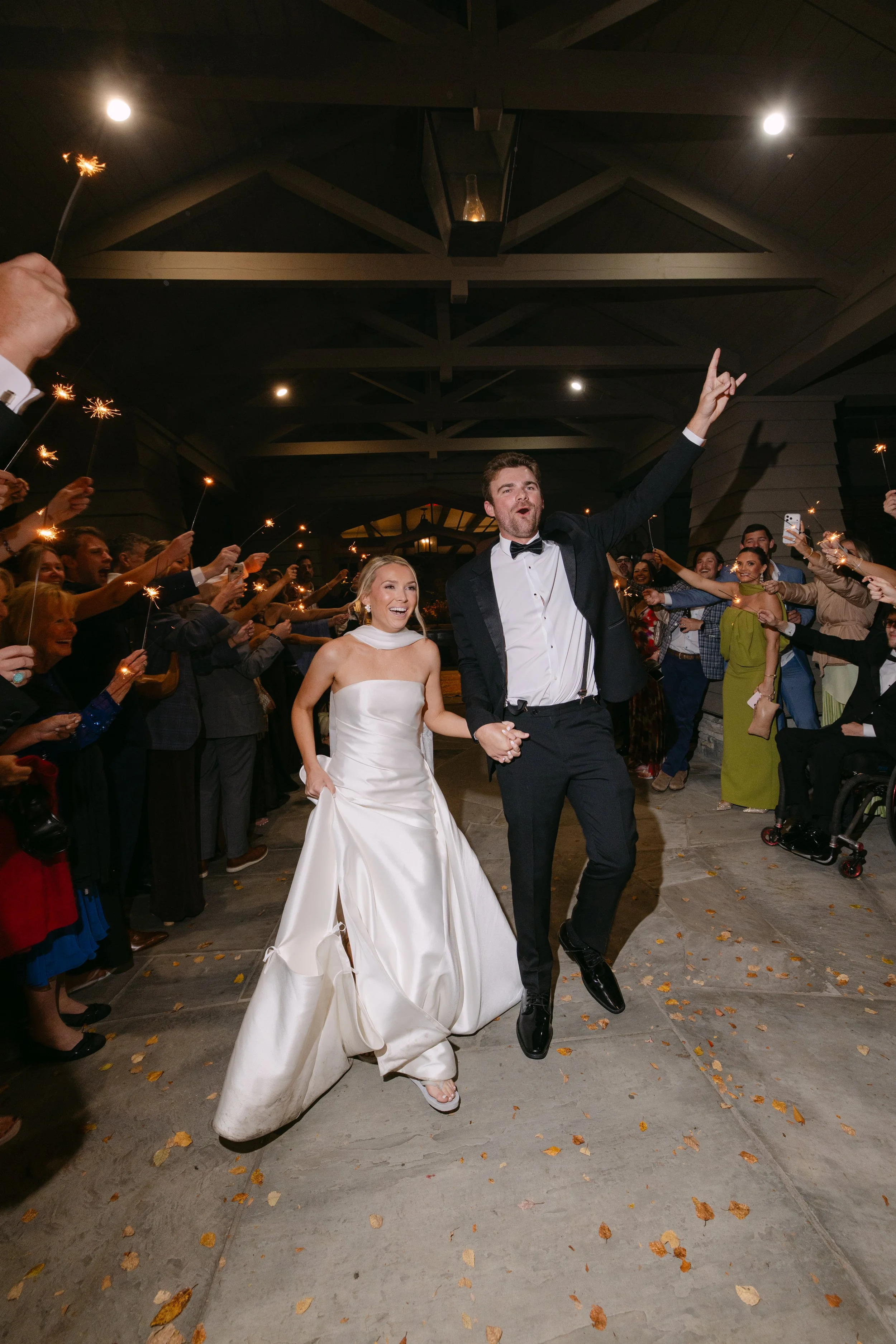Newlywed couple dancing at a wedding reception as guests hold sparklers and take photos.