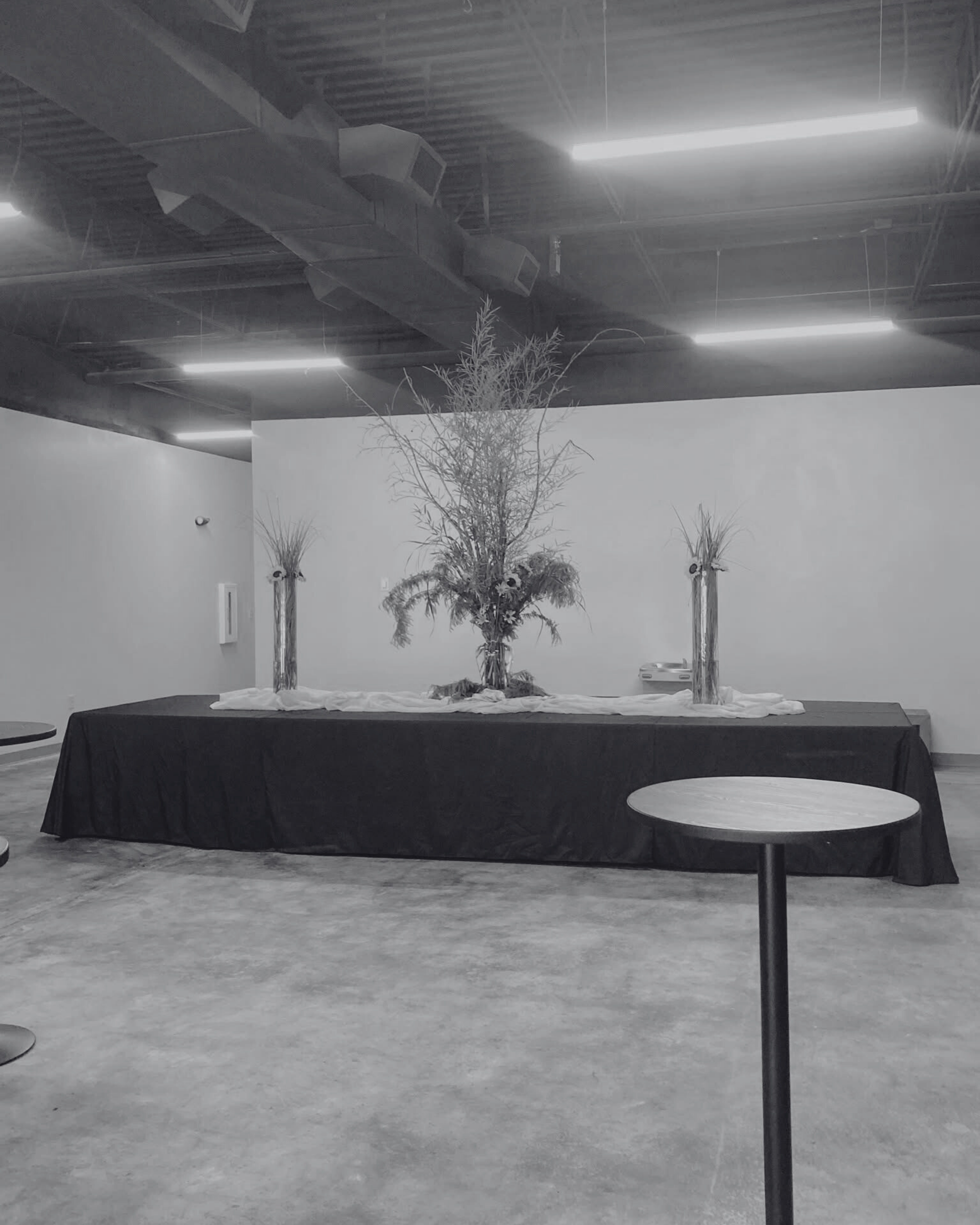 Empty room with minimalist decor, large table with floral arrangement, and a small round table in the foreground.