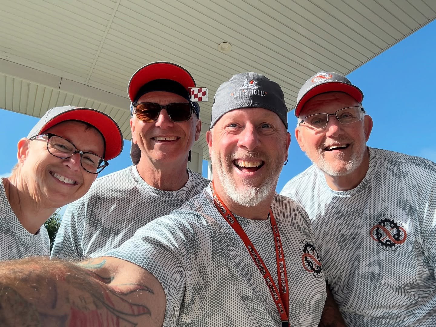 Four smiling Limitless Cycling volunteers wearing matching shirts and hats pose together outdoors on a sunny day. The image highlights community, teamwork, inclusion, and the dedicated volunteers who help create accessible outdoor experiences.