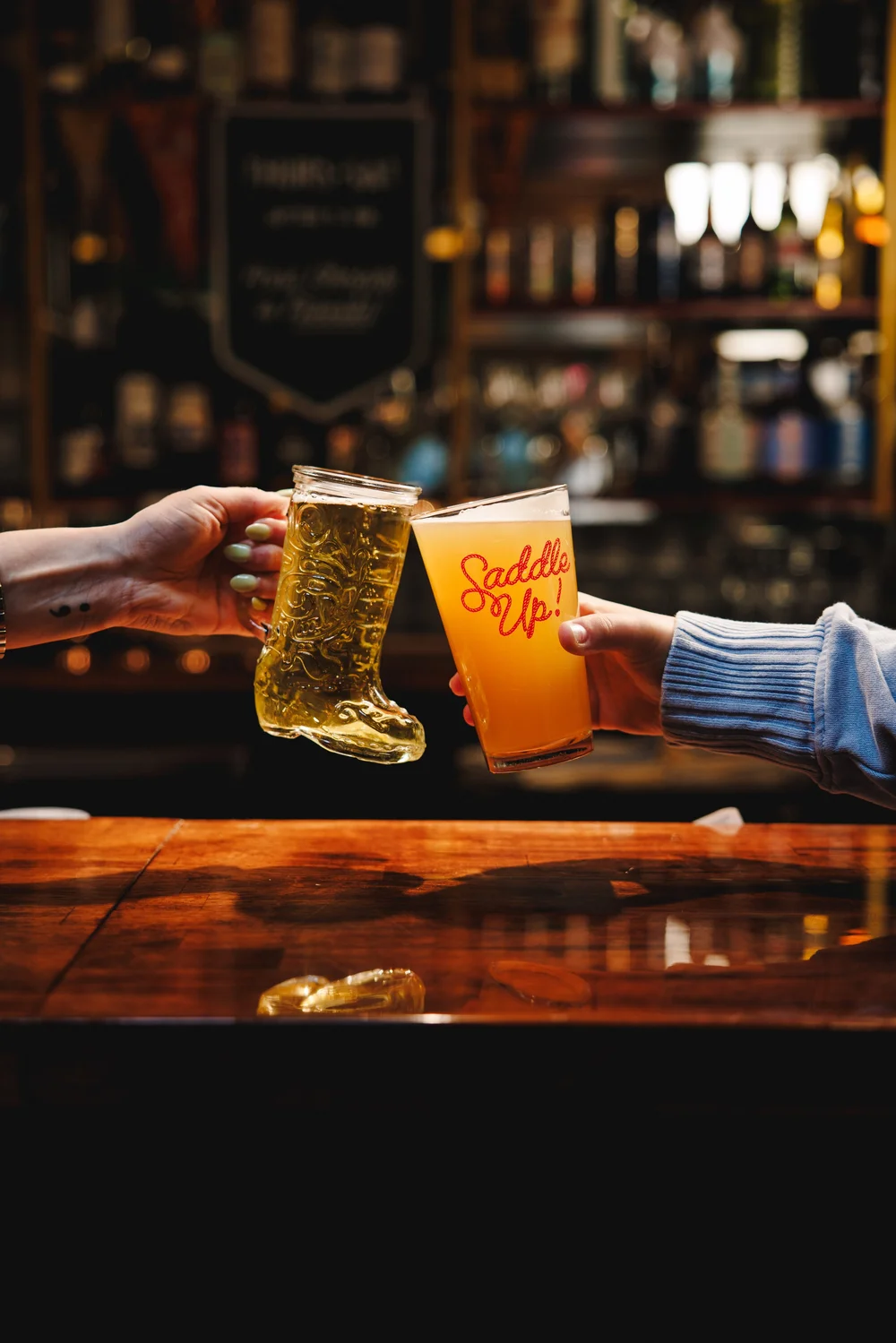A beer boot and Saddle Up glass raised at the bar in The Lodge at Front Range KC