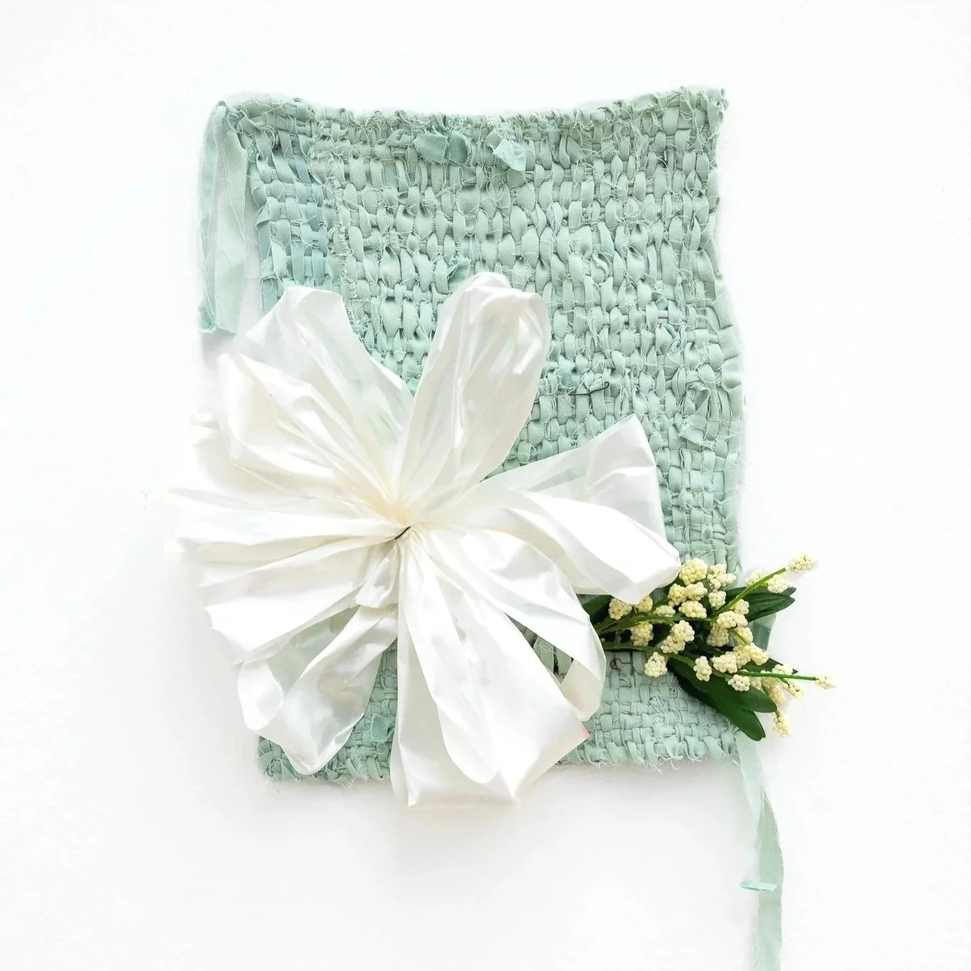 A teal weaving made of a medical gown, featuring a white bow and white flowers with green leaves.