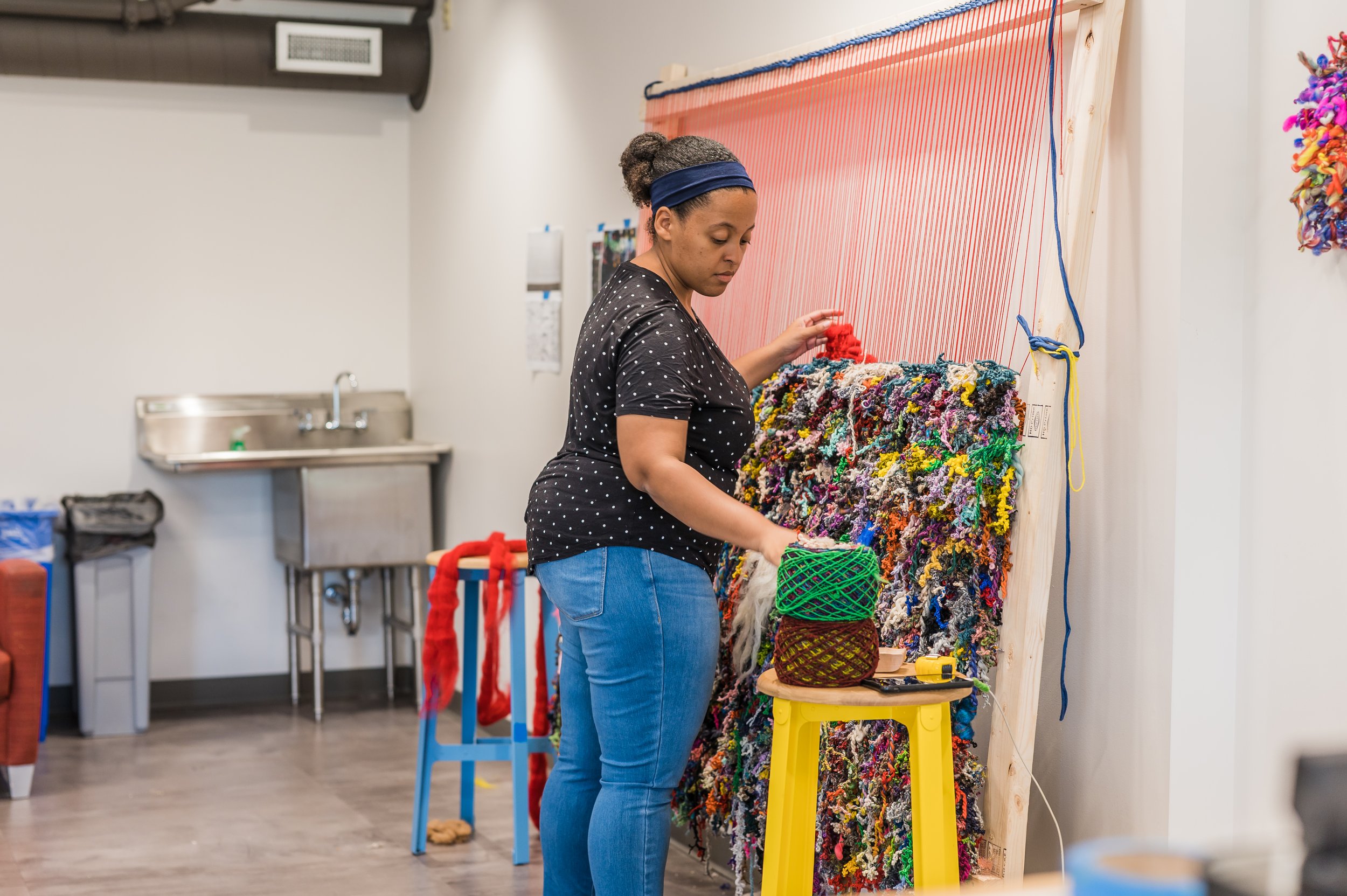 Woman working on a colorful, textured weaving wall art in an indoor studio.