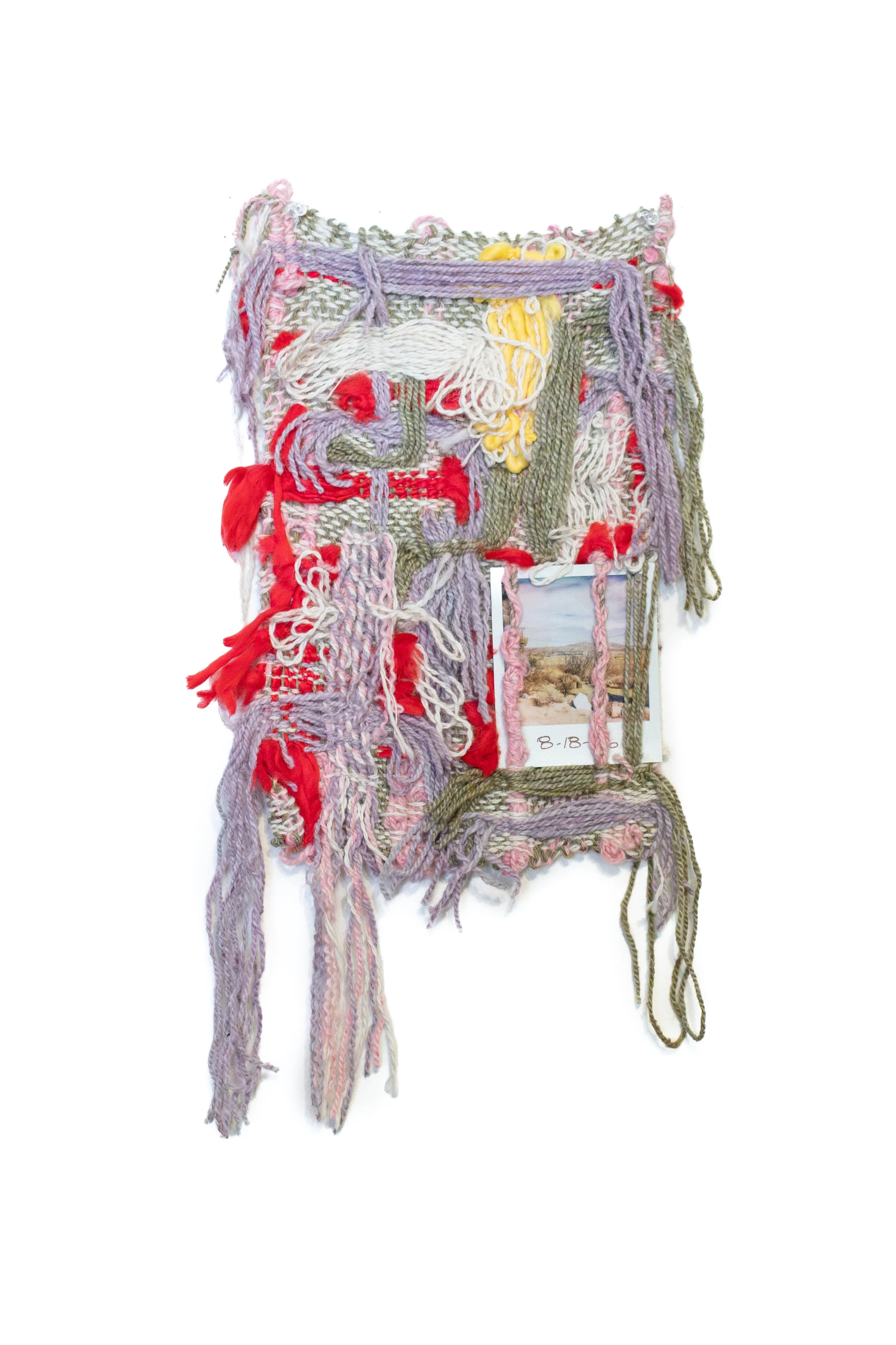 Colorful textile art piece made of various yarns and threads, intertwined and hanging on a wall, with a small landscape photo attached at the bottom.