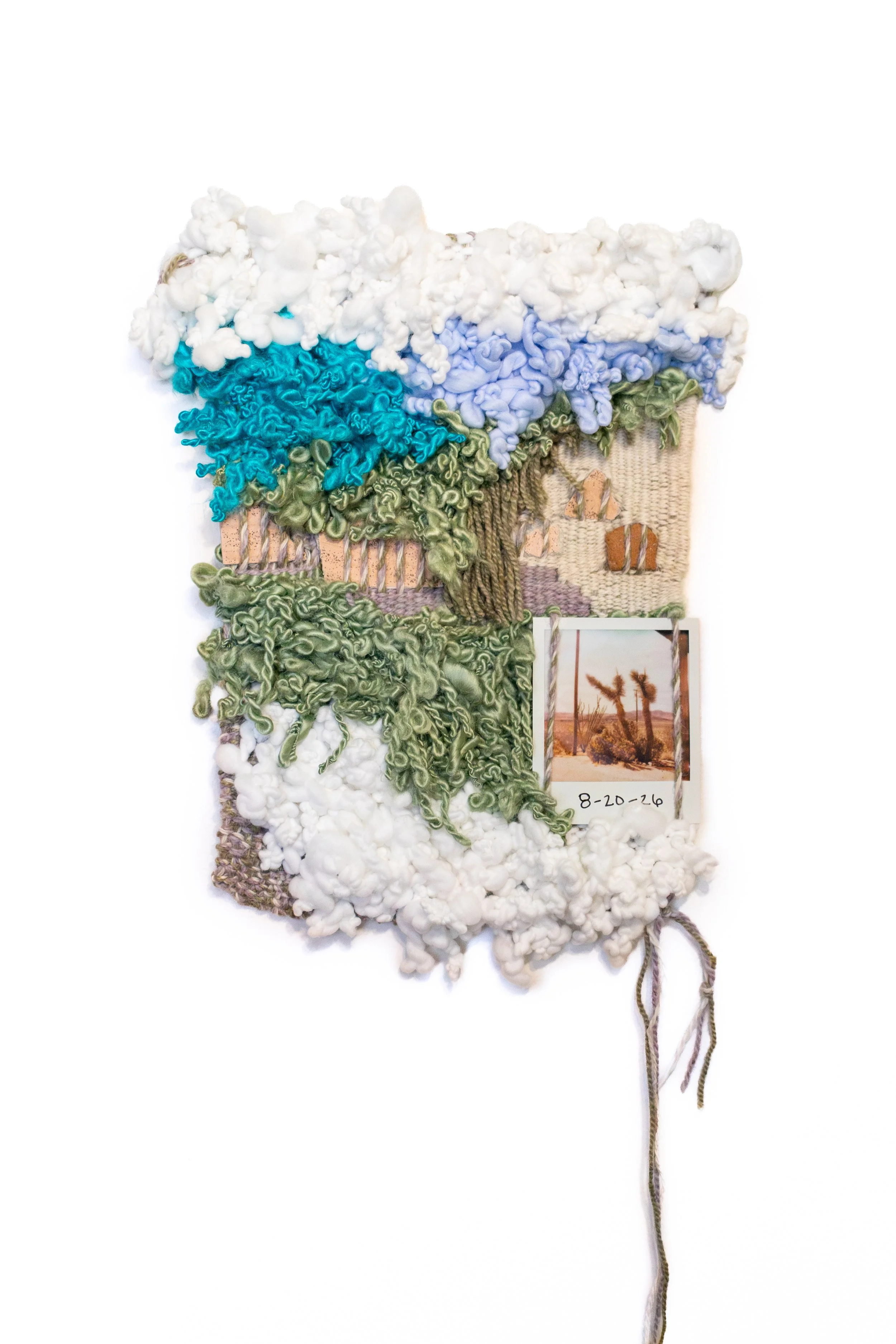 Mixed media textile art piece resembling a landscape with clouds, trees, and a mountain, featuring various textured fabrics and small printed photo, dated 8-20-26.