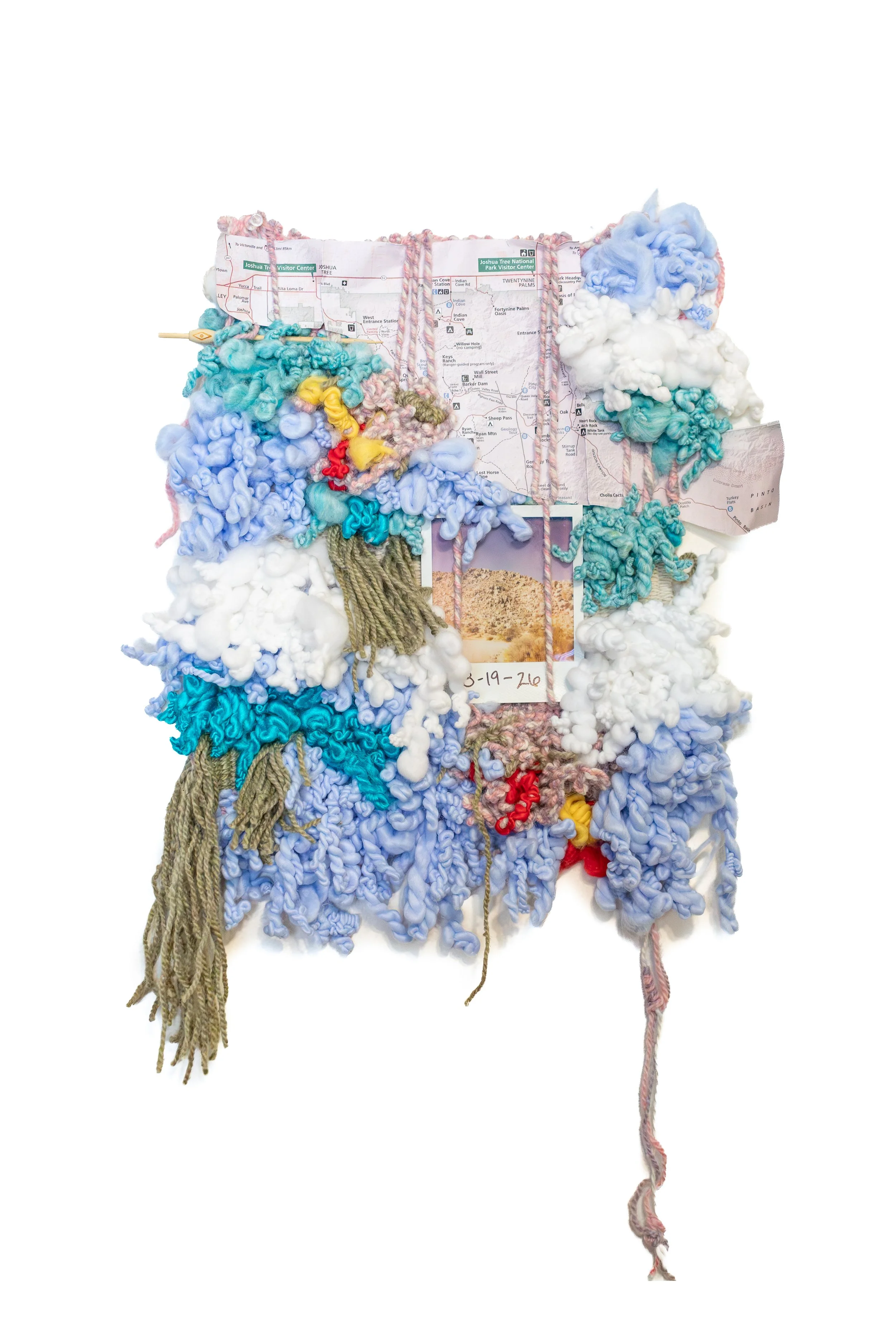 A mixed-media art piece featuring a map of Joshua Tree National Park covered with colorful, textured yarn and fabric, with a photograph dated with writing at the bottom.