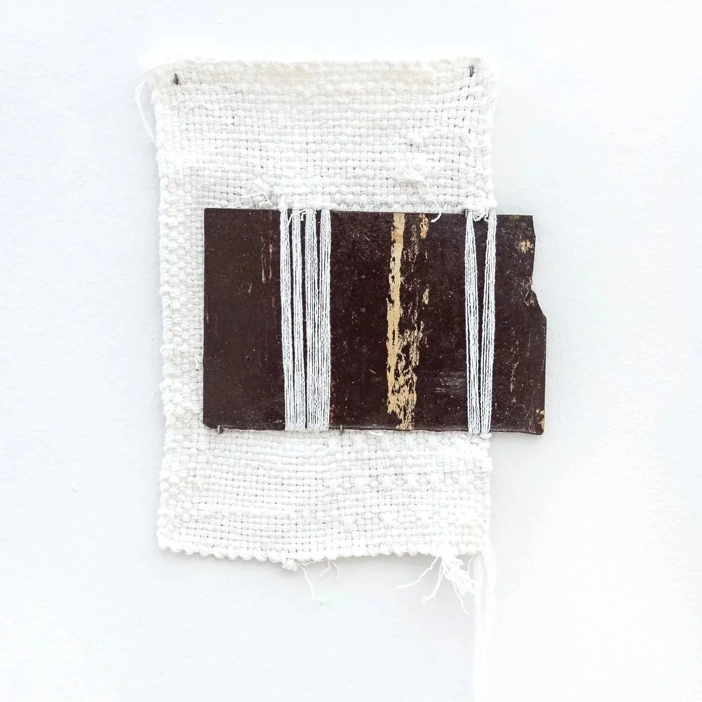 A white cotton weaving with a brown rectangular tile inserted on the right side.