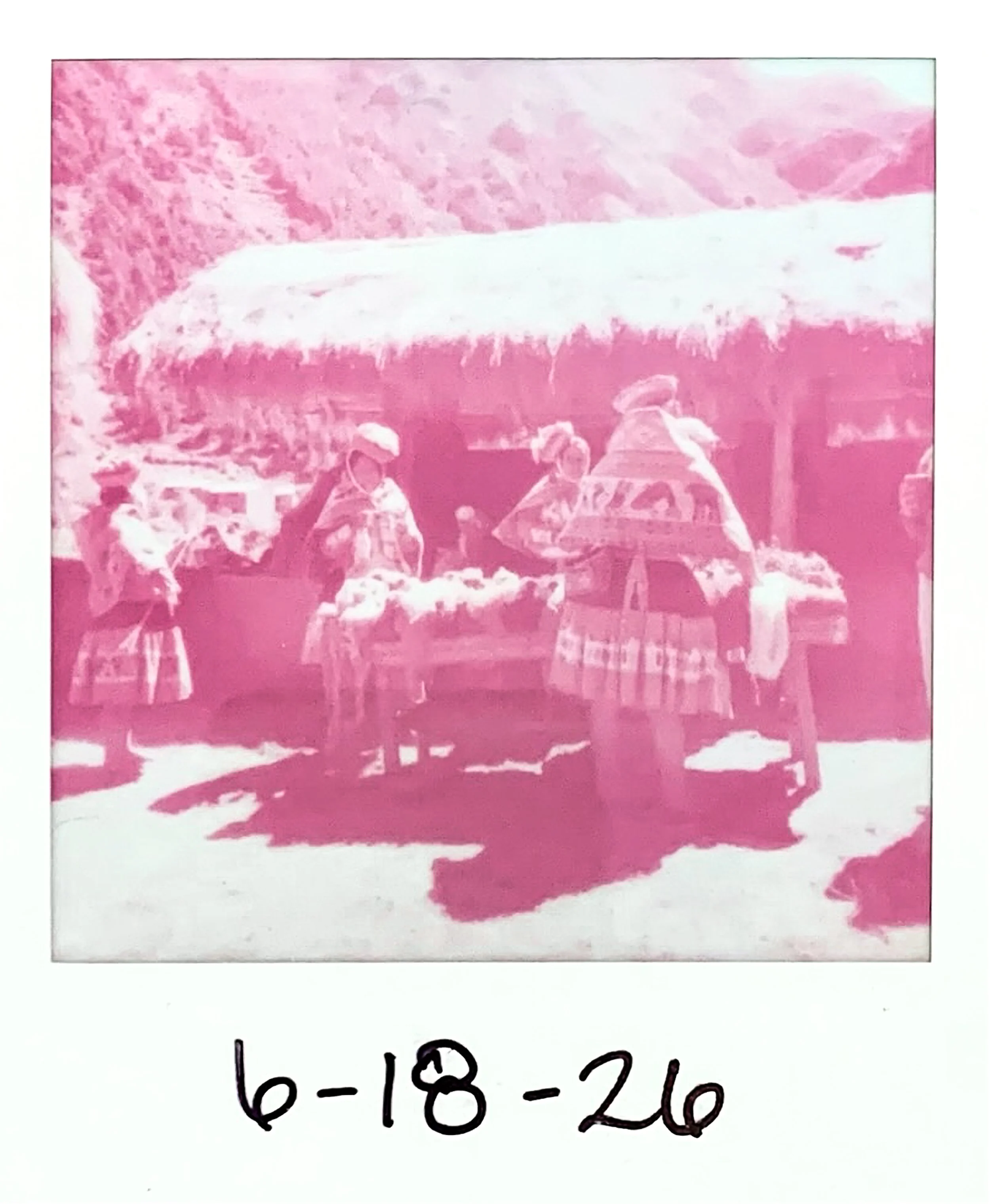 A pink-tinted photograph of Quechua weavers gathering around a table. The scene appears to be a community event that is dated '6-18.26'.