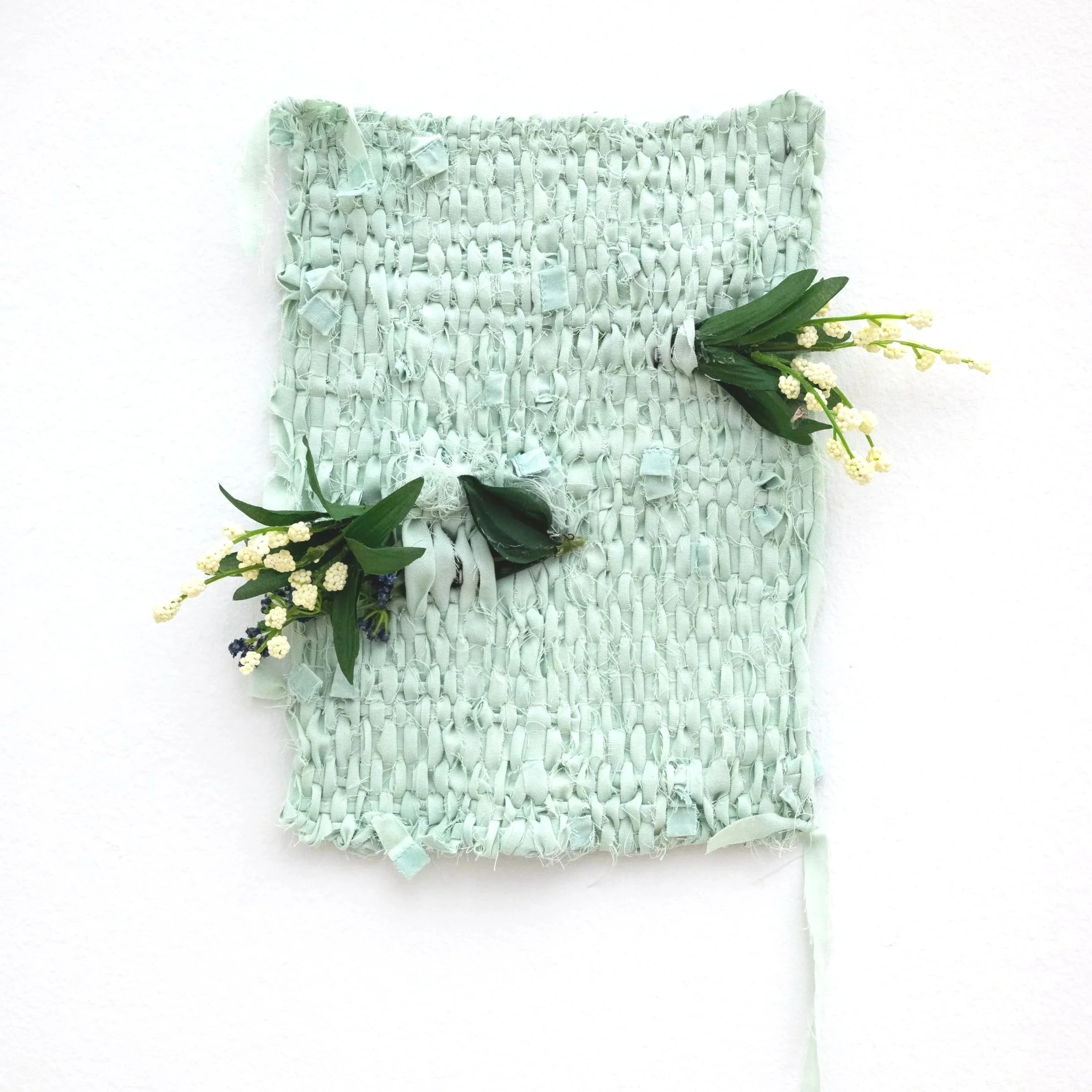 A teal weaving made of a medical gown, featuring white and purple flowers and green leaves.