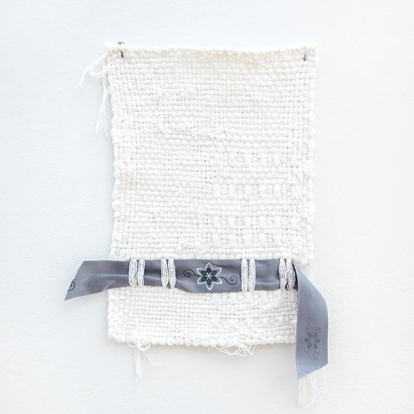 A white cotton weaving with a gray and blue ribbon inserted through the bottom.