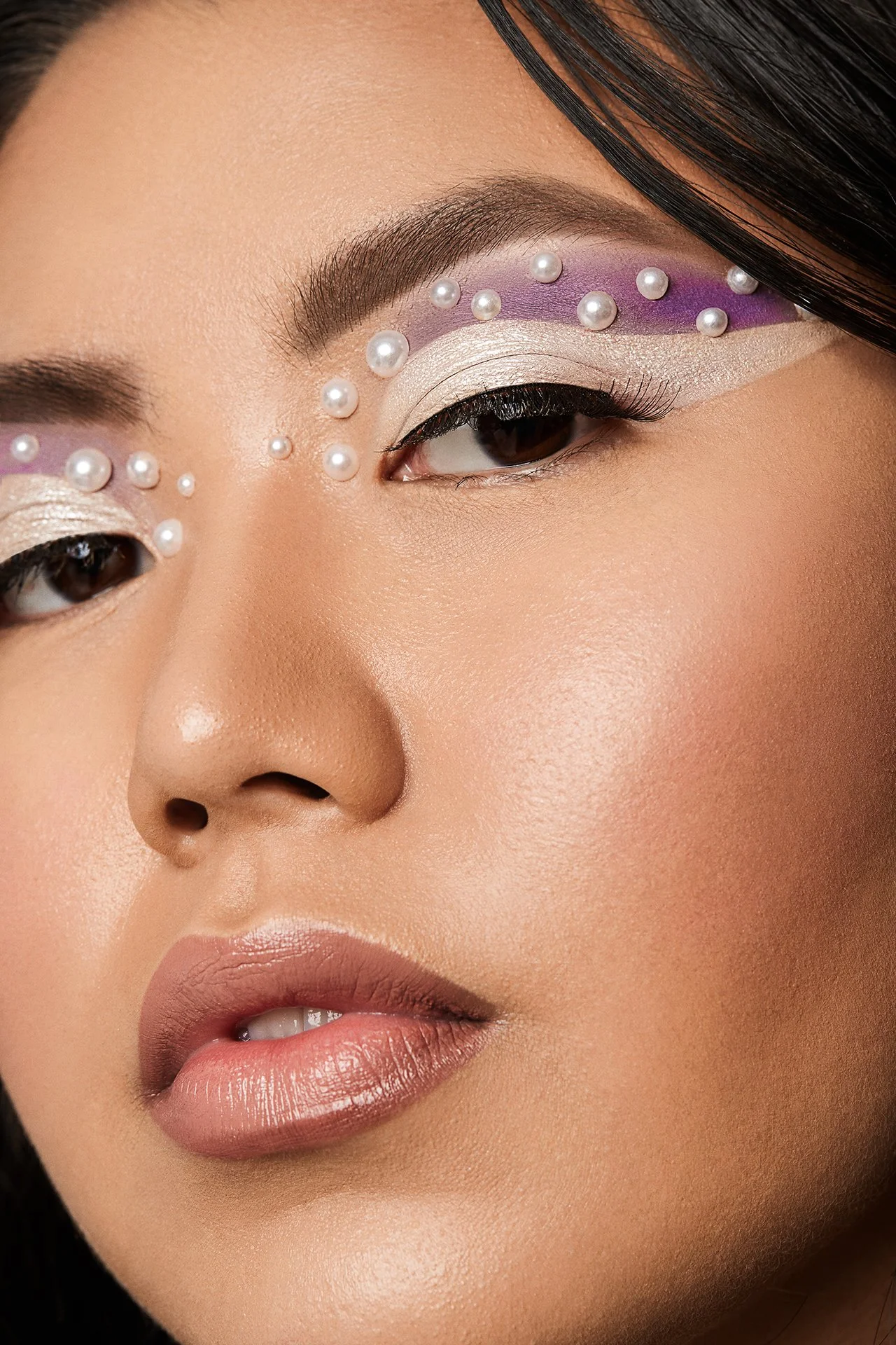 Close-up of a woman's face with pearl-studded eye makeup and bold eyeshadow.