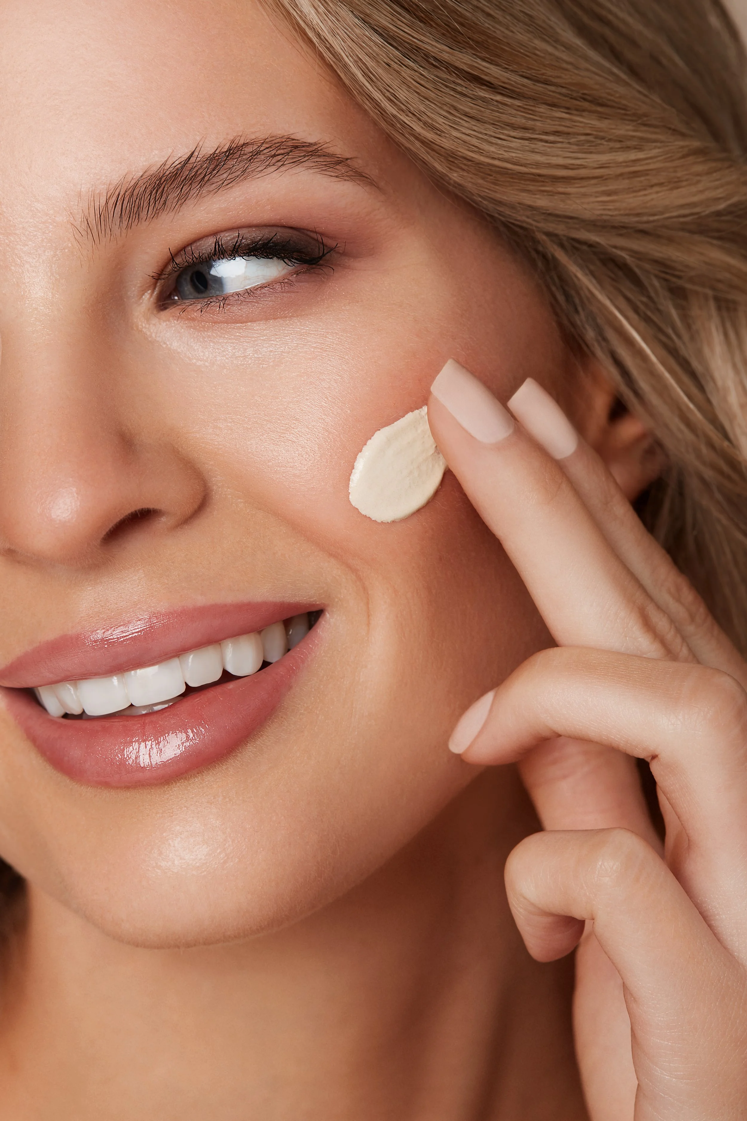 Close-up of woman applying cream to her cheek, smiling.