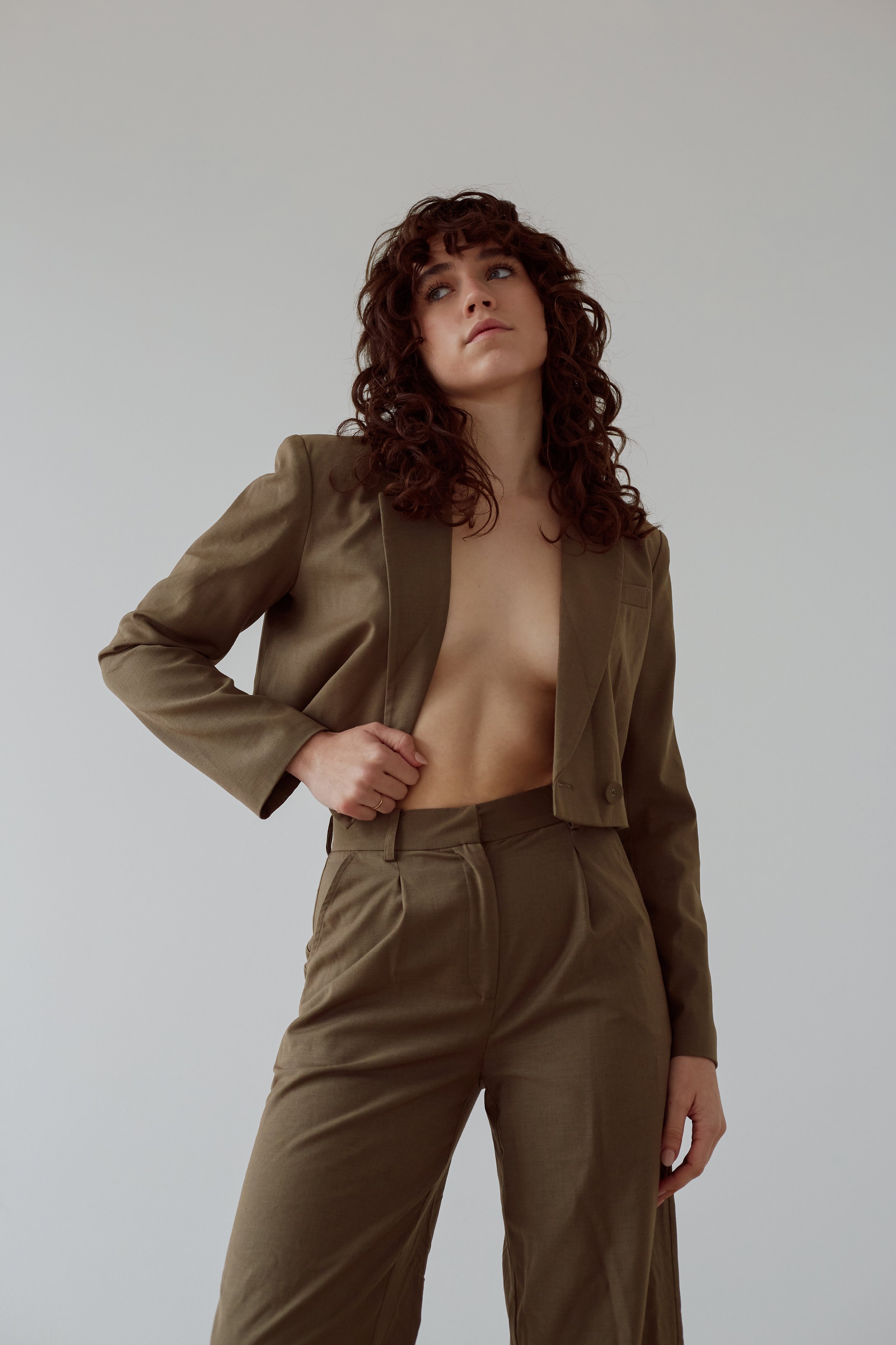 Person wearing an olive green suit with long curly hair looking upwards.
