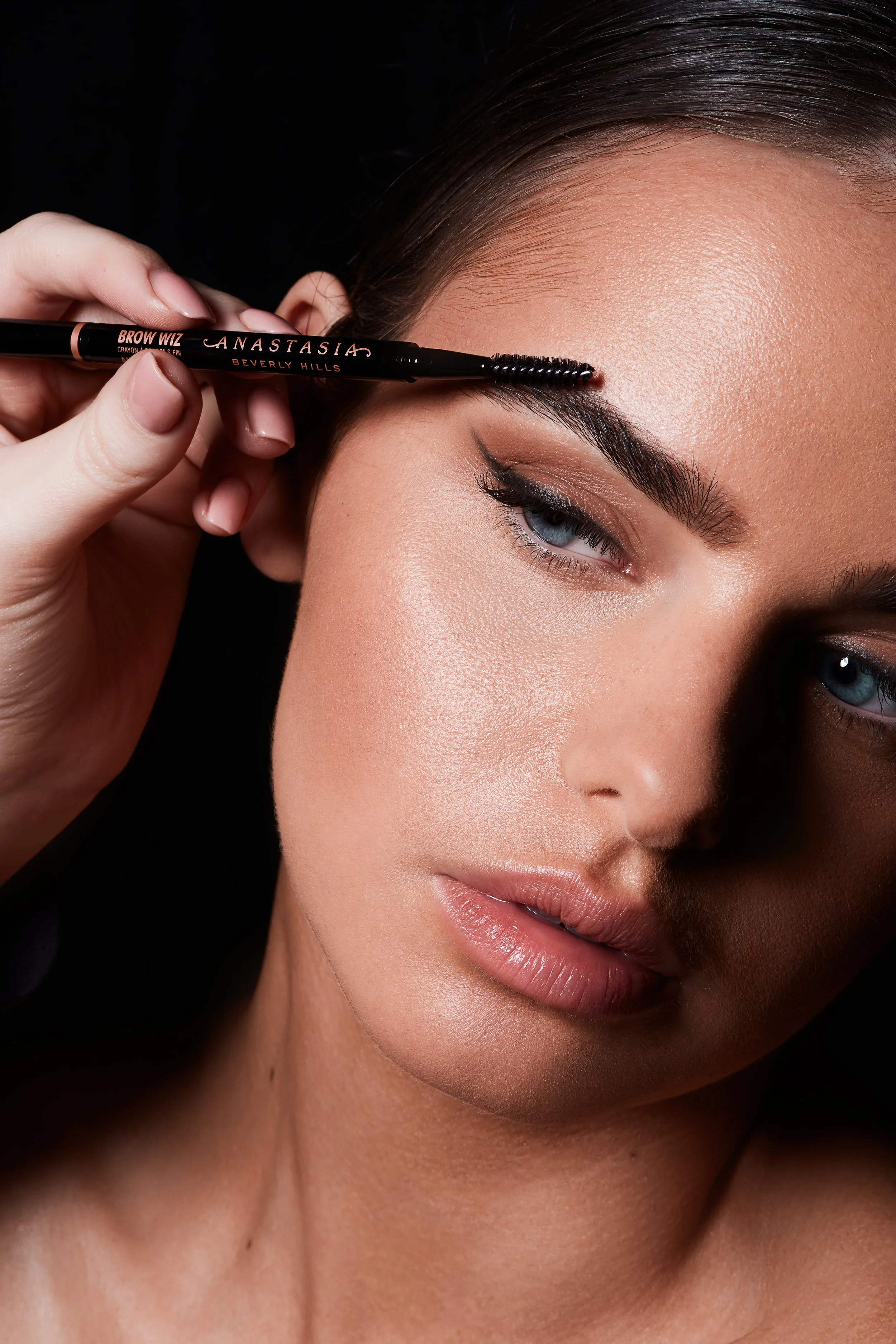 Woman applying eyebrow pencil to groom eyebrows, featuring "Anastasia Beverly Hills Brow Wiz."
