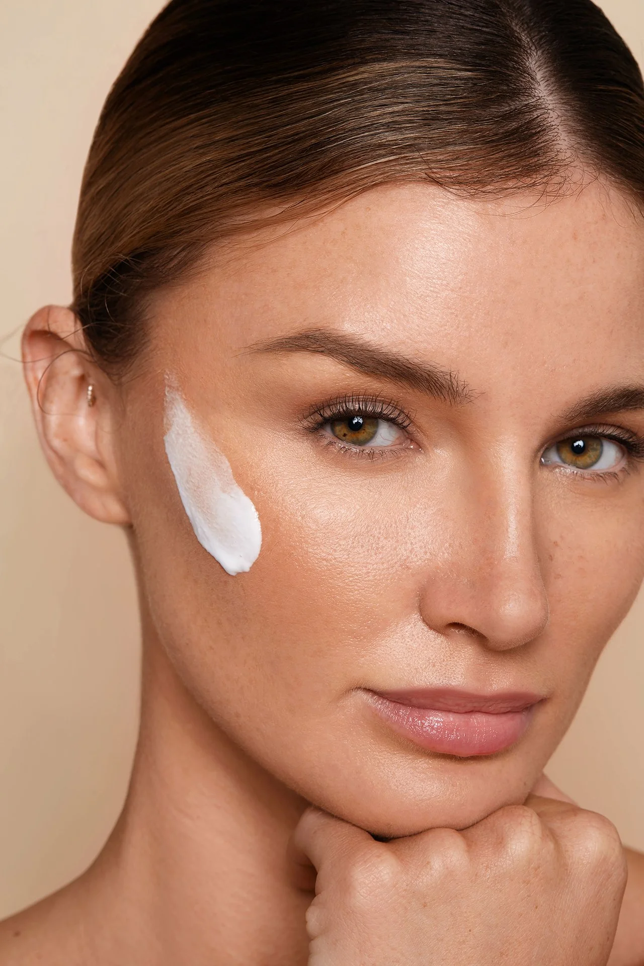Close-up of a woman with skincare cream on her cheek.