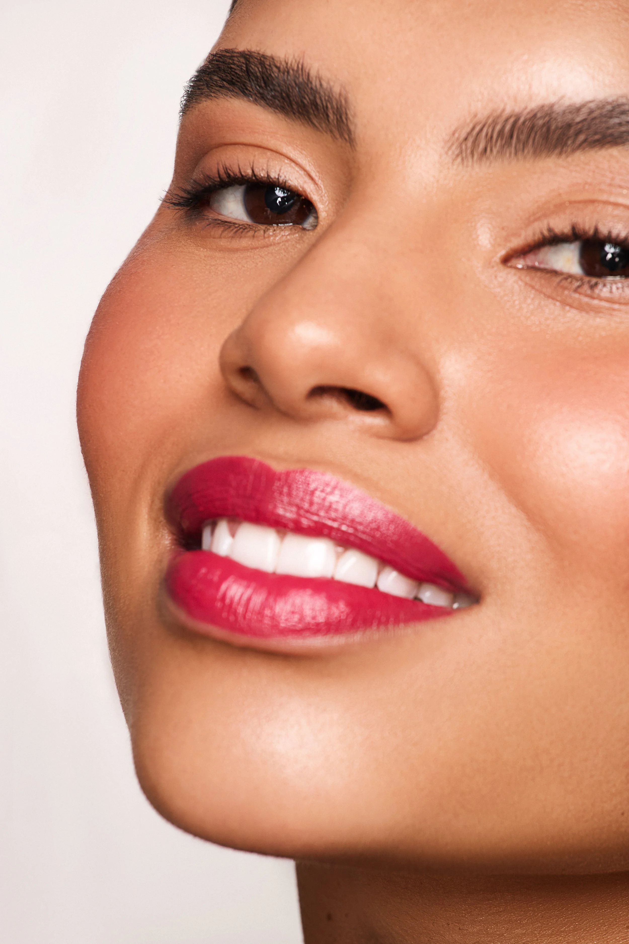 A close-up of a smiling woman with makeup, including pink lipstick, and well-groomed eyebrows.