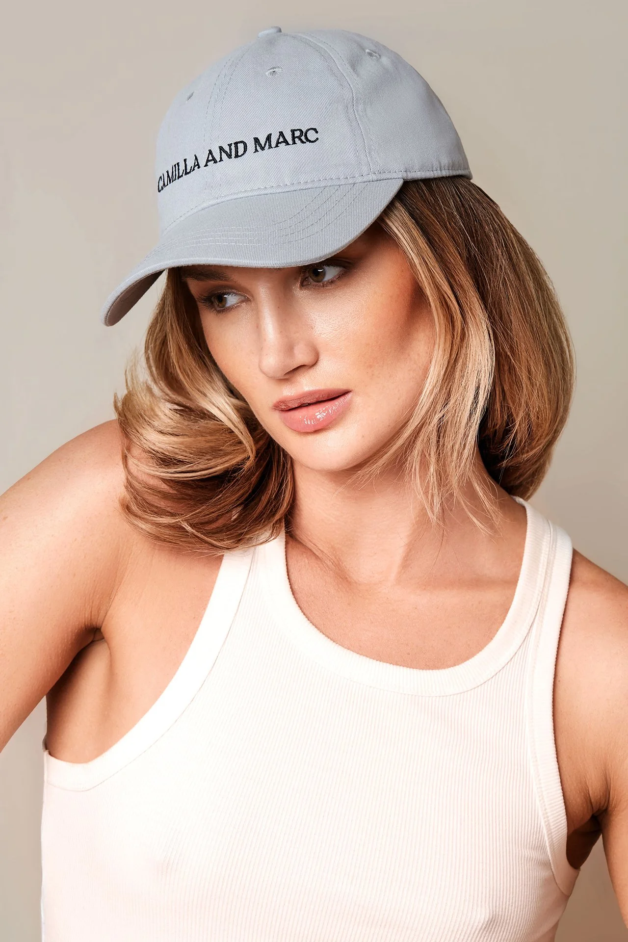 Person wearing a light blue baseball cap with "CAMILLA AND MARC" text, and a white tank top.