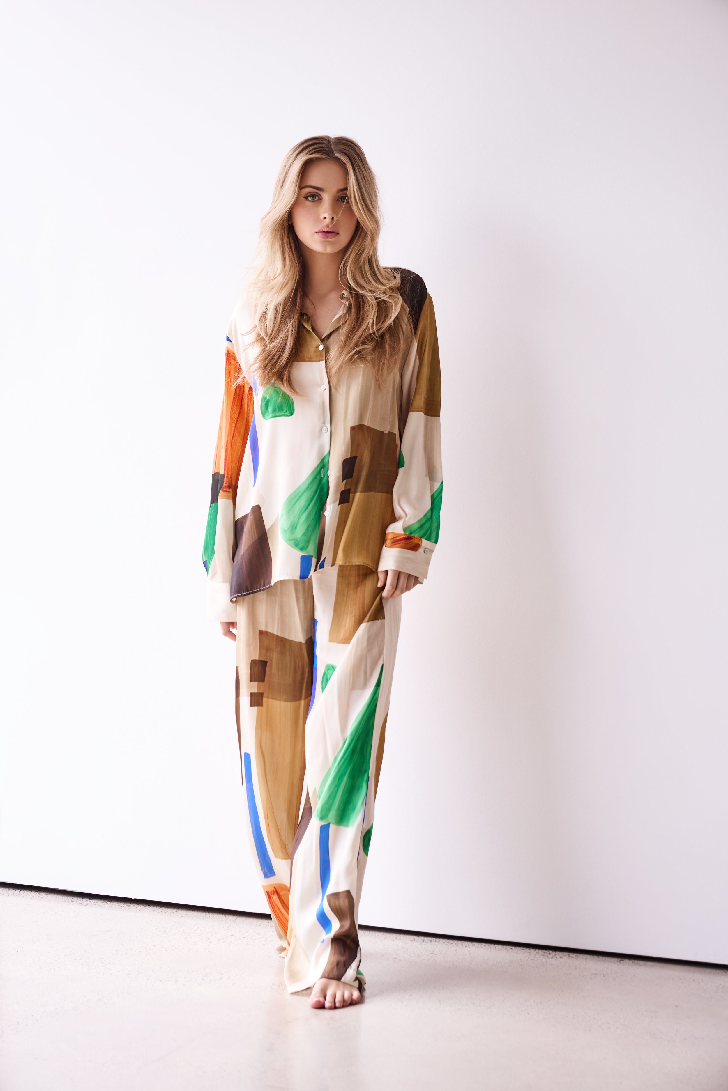 Woman wearing colorful abstract print pajamas standing on a white floor against a plain white wall.