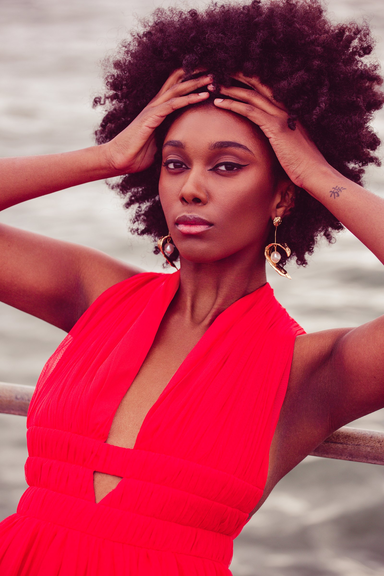 Woman in a sleeveless red dress holding her head, wearing large earrings.