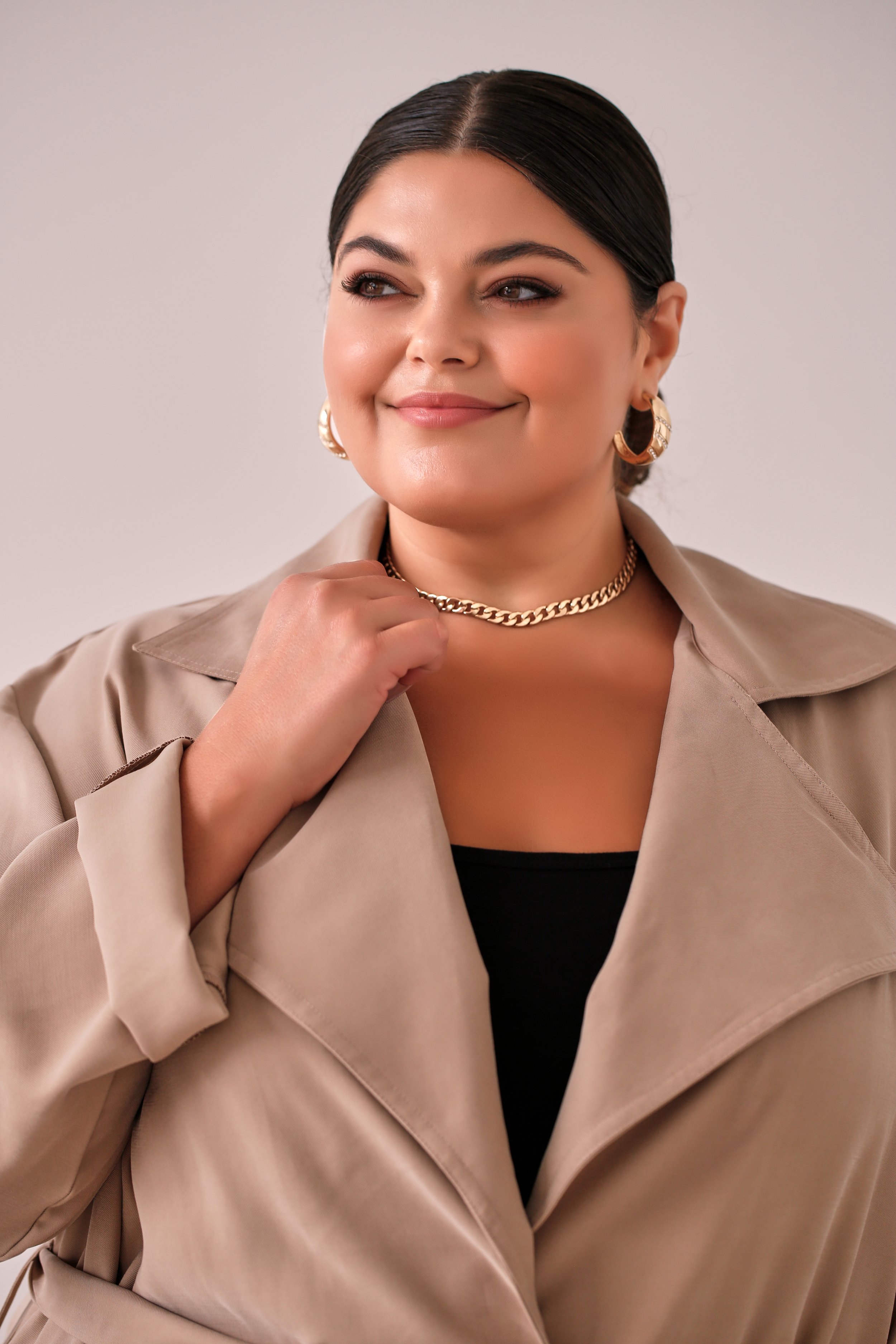Woman wearing beige coat, gold chain necklace, and hoop earrings