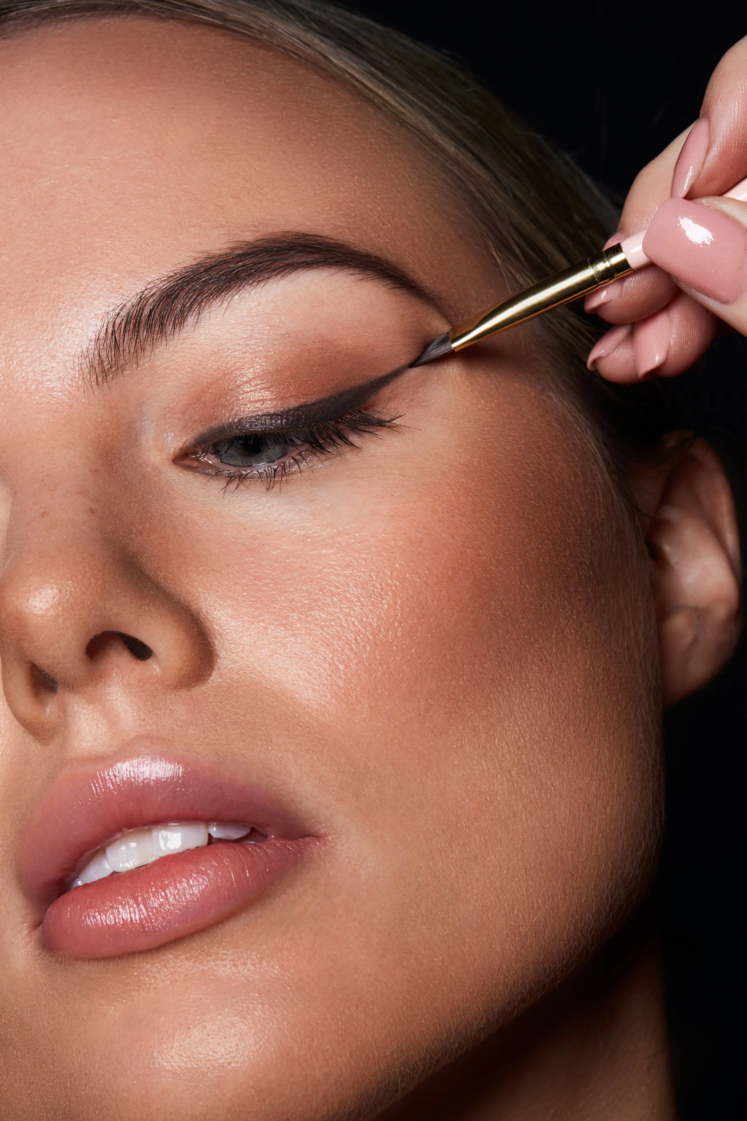 Close-up of a person applying black eyeliner with a brush to the upper eyelid