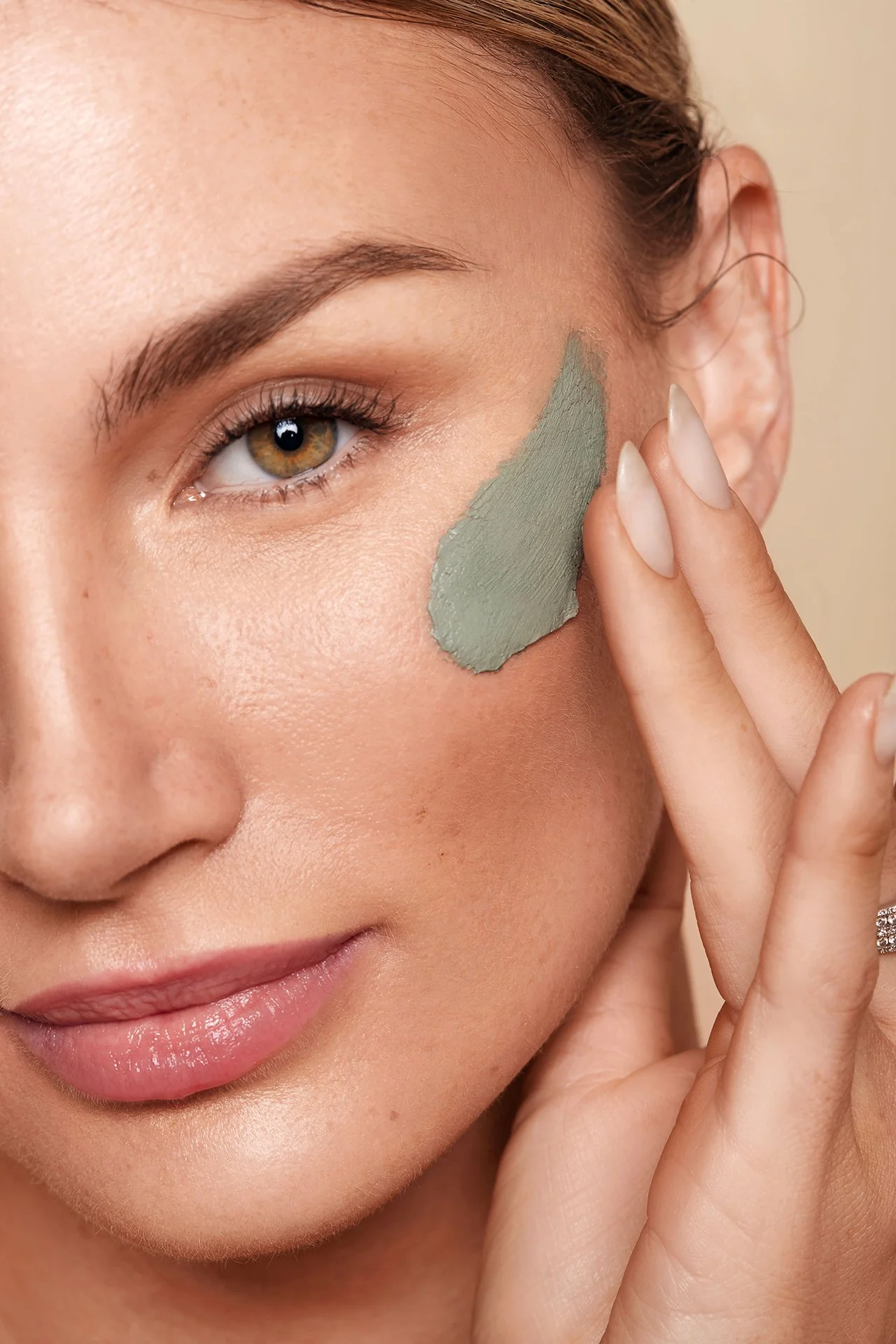 Close-up of a woman applying green clay mask on her cheek