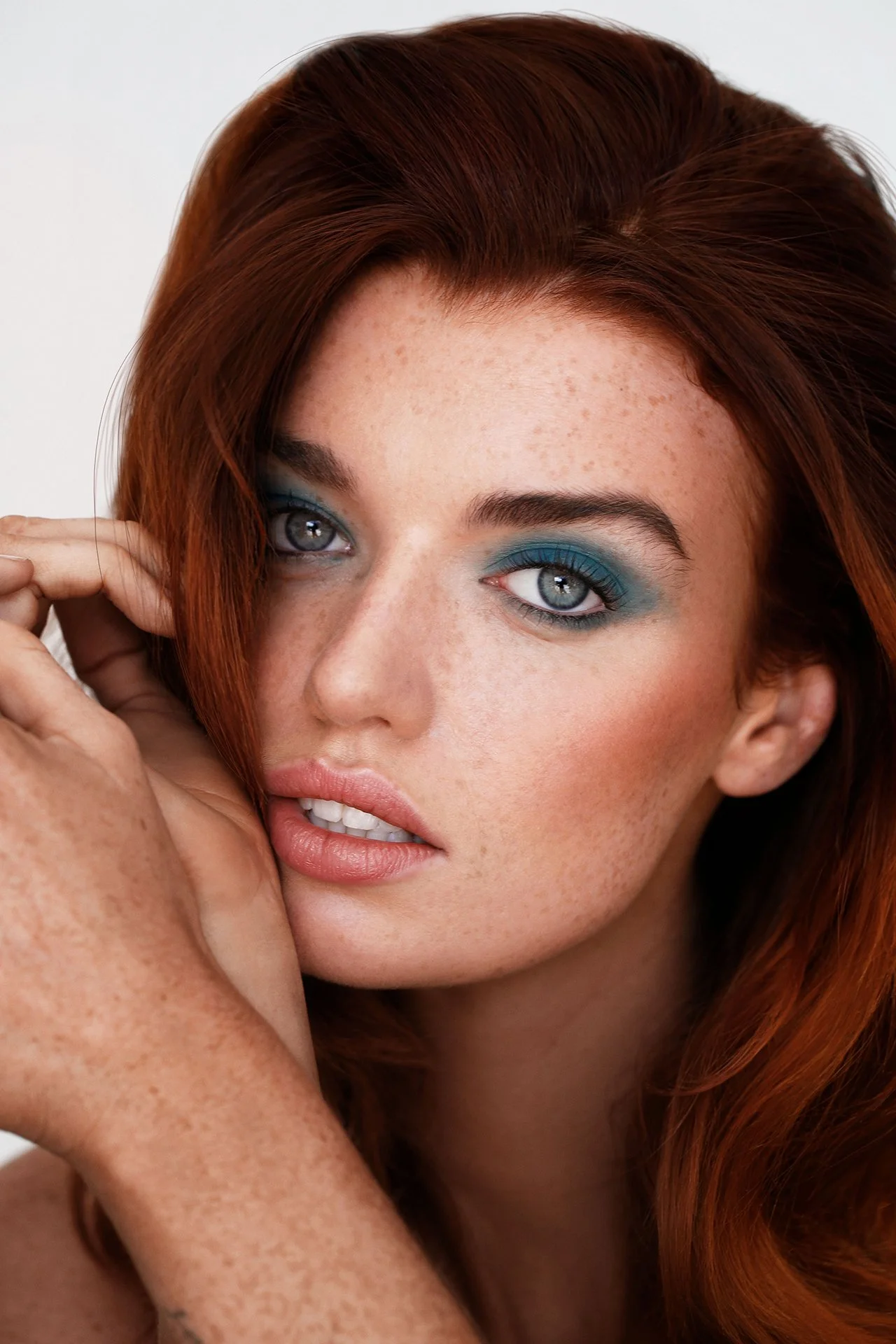 Close-up of a woman with red hair, blue eyeshadow, and freckles.