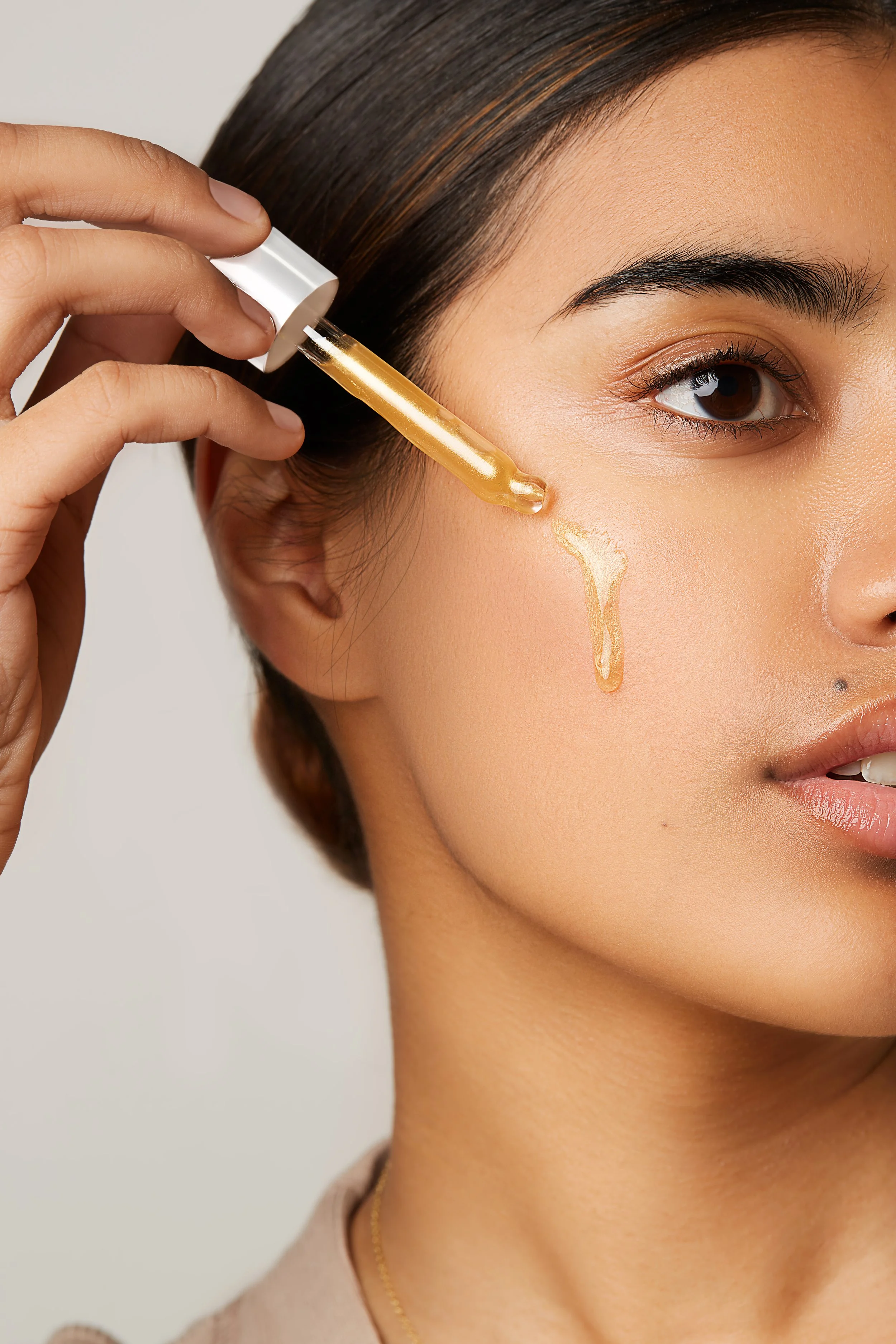 Close-up of a woman applying serum on her cheek with a dropper