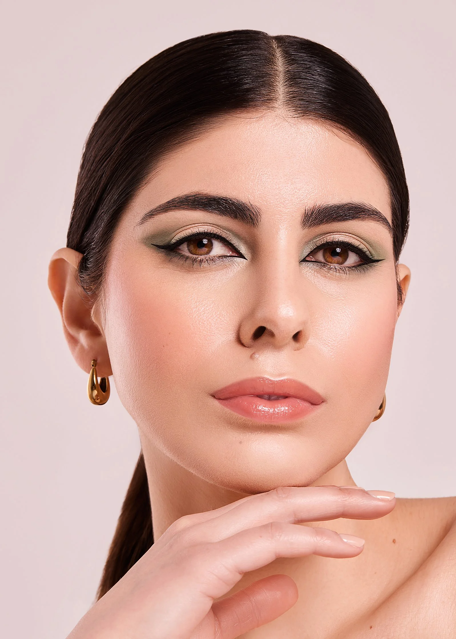 Close-up of a woman with green eye makeup and gold hoop earrings.