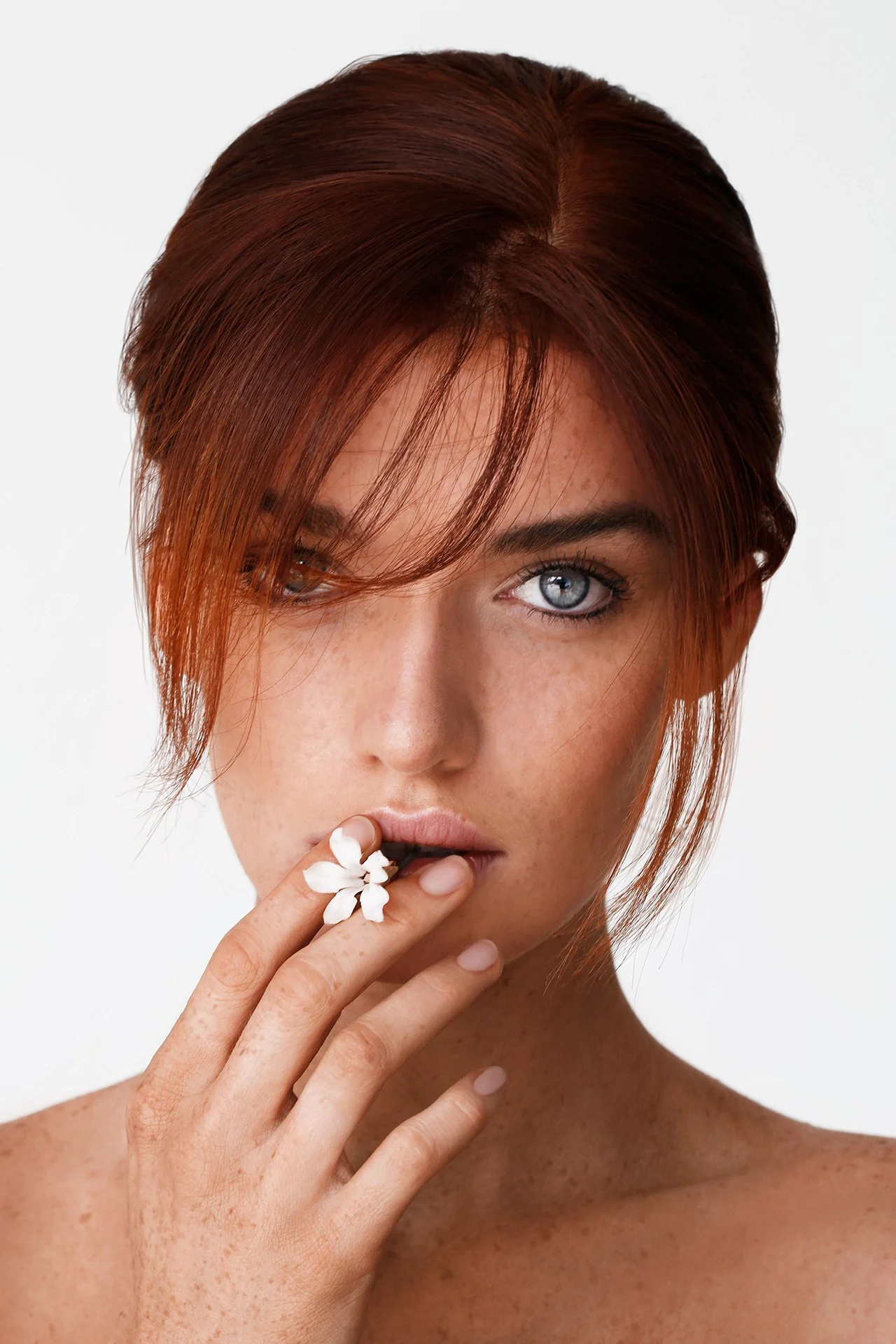Woman with red hair holding a white flower to her lips