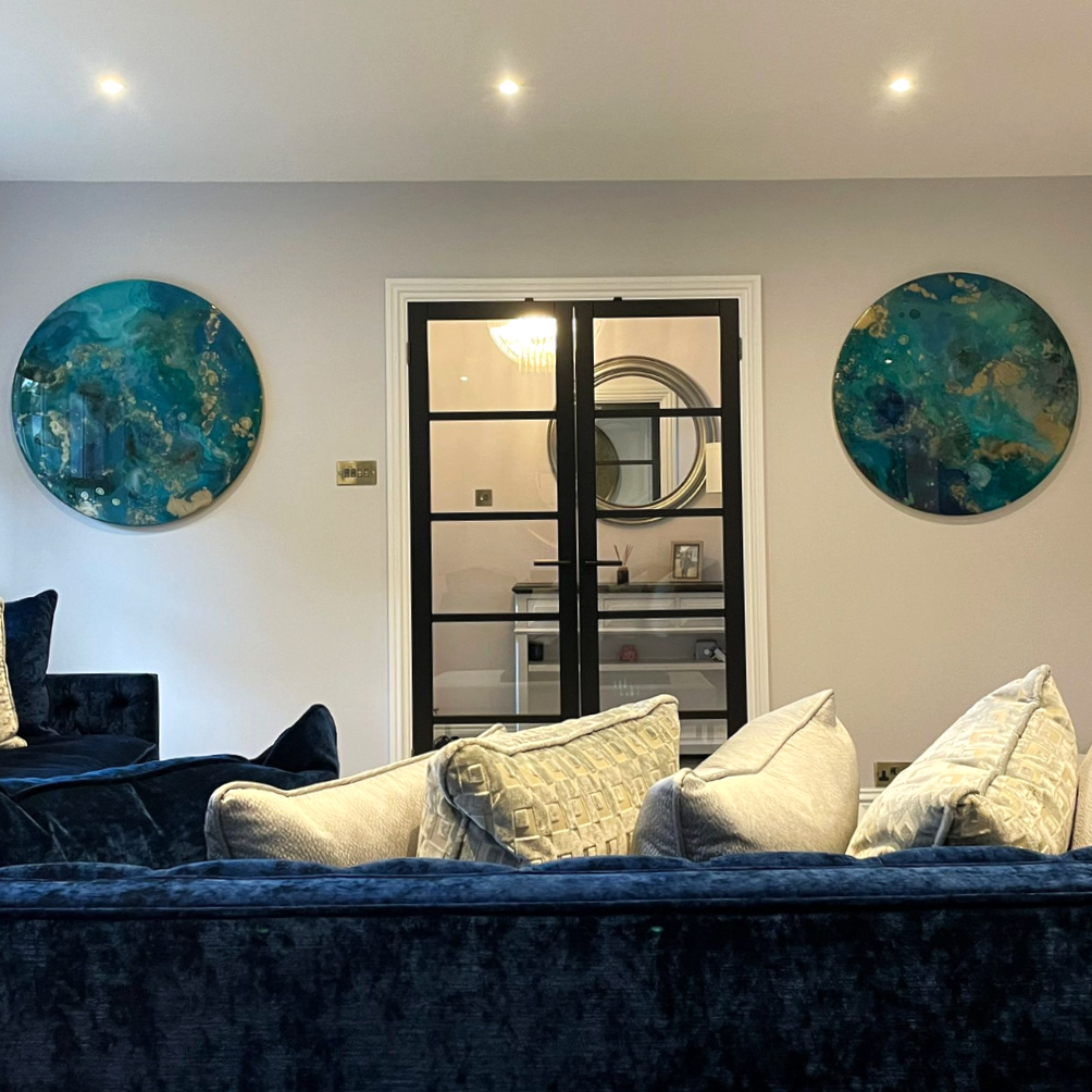 Living room with a navy velvet sofa and beige cushions, two round abstract Brown black copper gold metal resin circle mixed media abstract interior large custom wall art designs made Katie Alize resin artist Essex London UK, paintings with blue, gree
