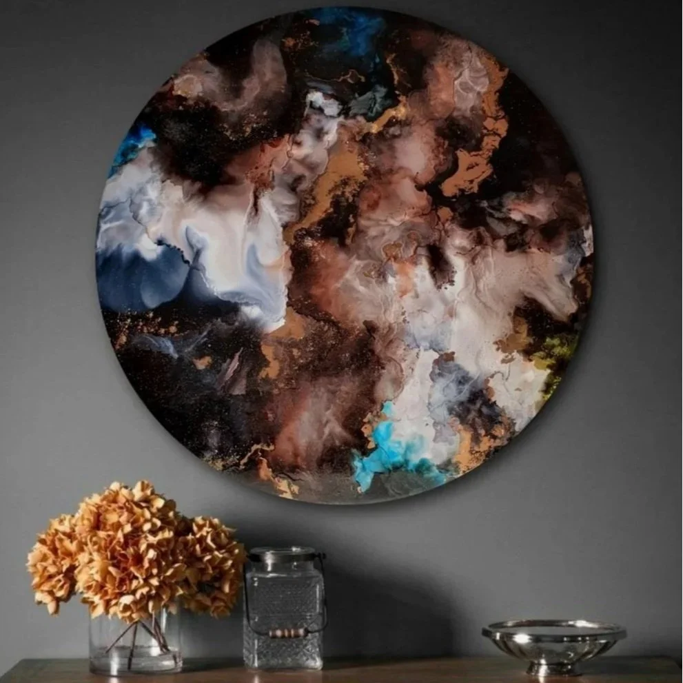 Abstract circular wall  resin alcohol ink circle mixed media abstract interior wall art designs made Katie Alize resin artist Essex London UK art with swirling colors of black, white, blue, gold, and brown, above a wooden console table with a vase of