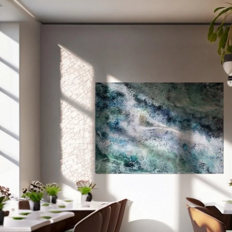 A modern dining room with sunlight casting shadows on the wall, featuring abstract art with blue, green, and white tones and a table set with flowers and tableware.  Abstract ocean resin mixed media artwork created by UK based artist Katie Alize