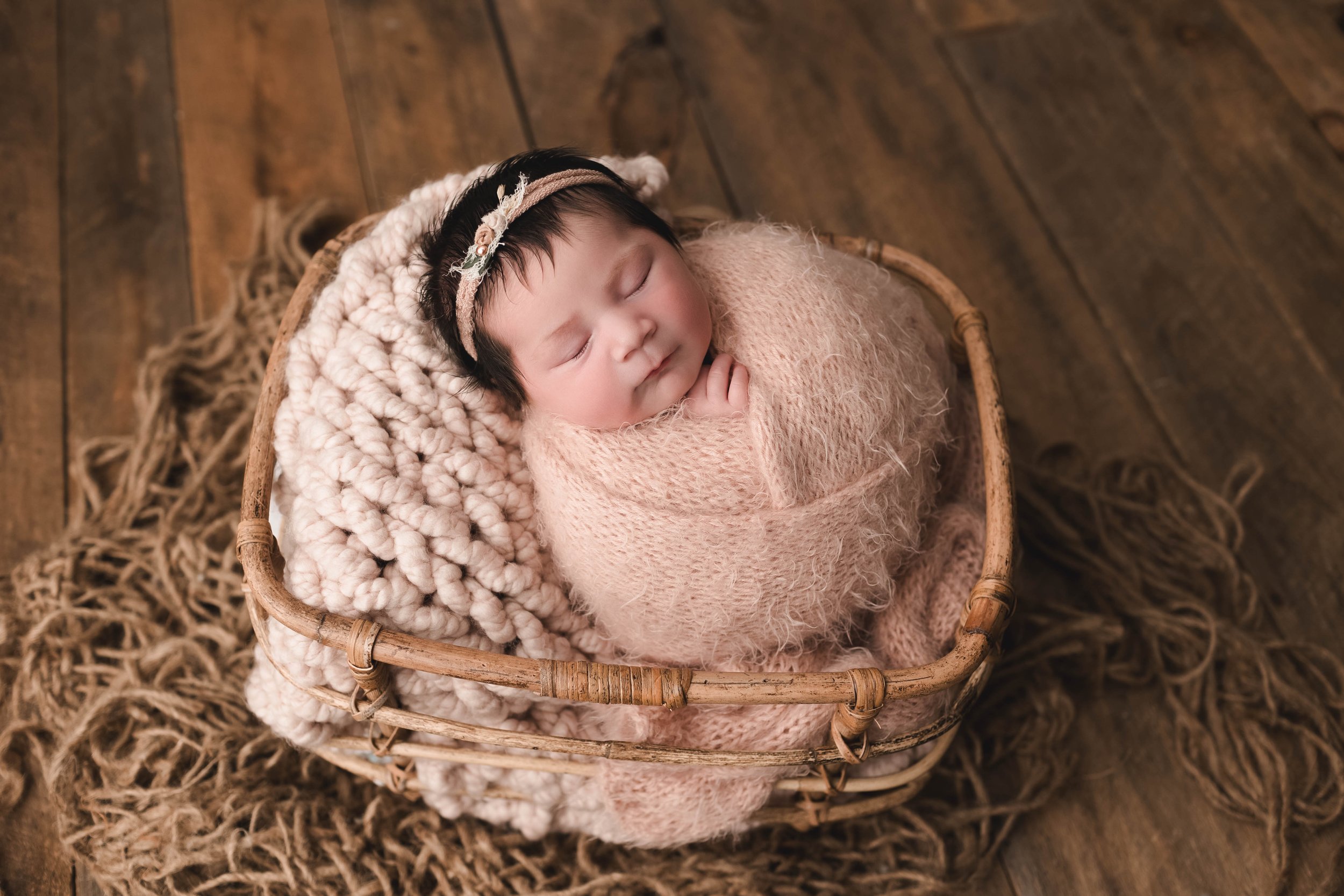 Wrapped newborn baby girl in basket on wood backdrop