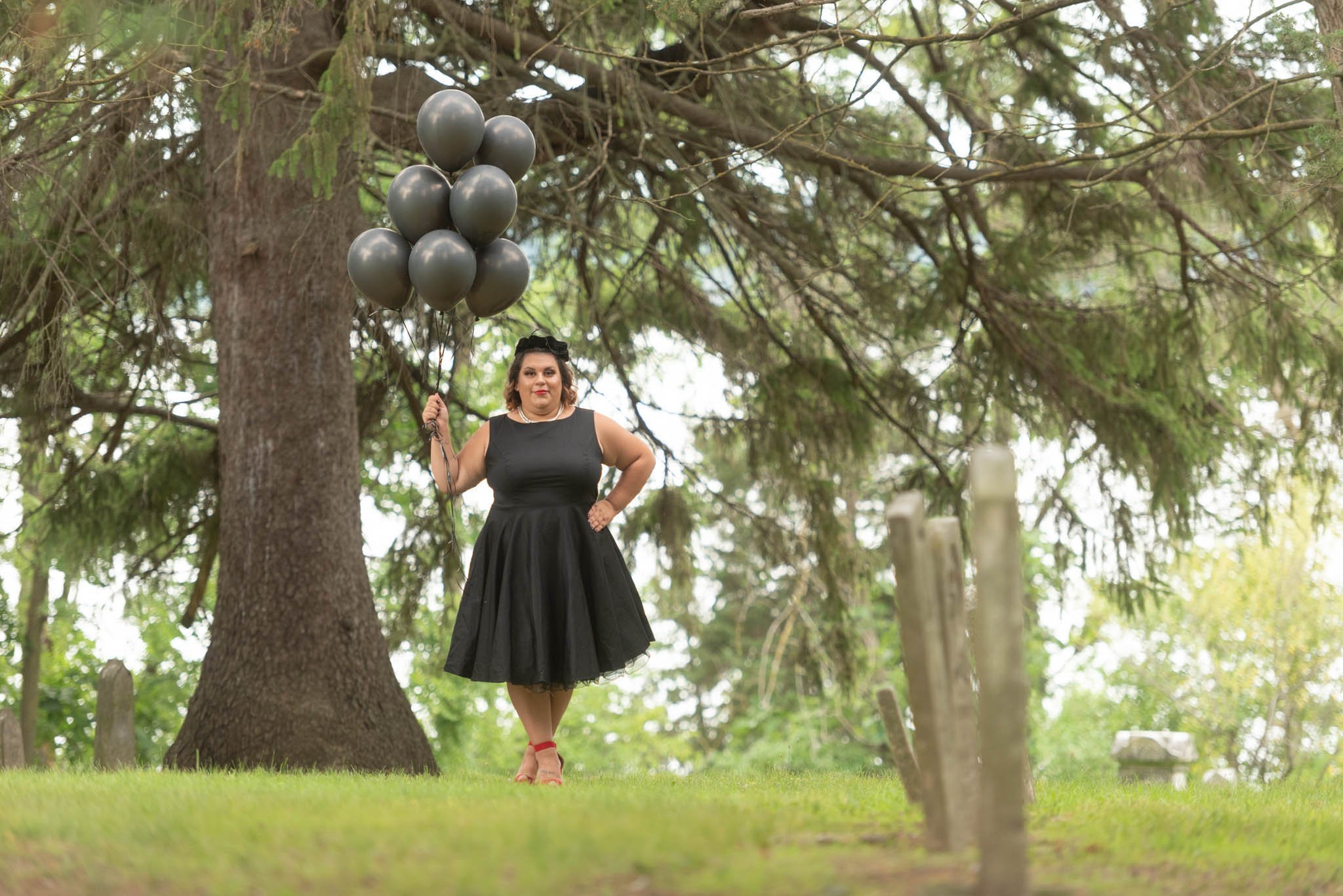  Samantha in black dress and vintage black hat poses in cemetery with black balloons.  