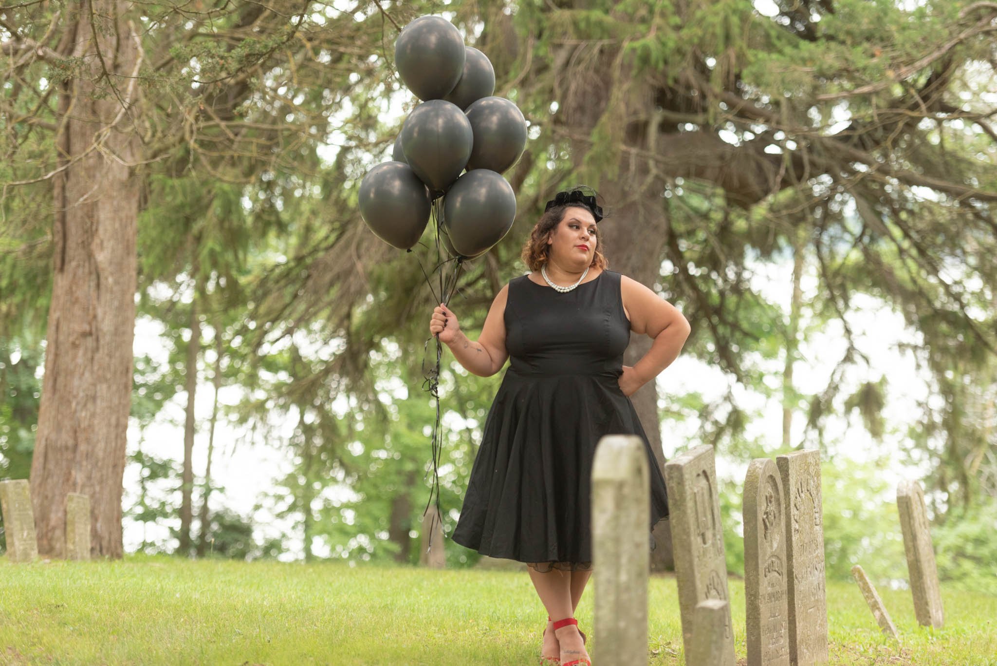  Samantha in black dress and vintage black hat poses in cemetery with black balloons.  