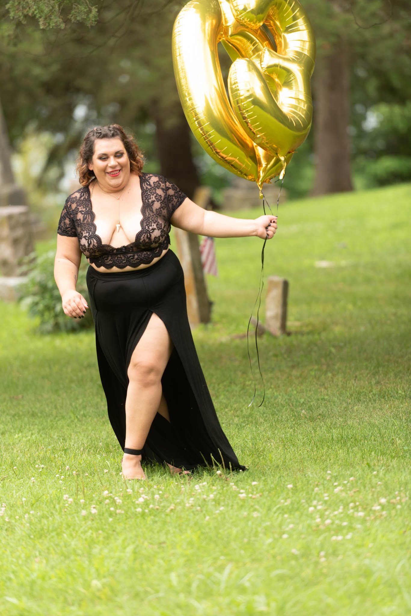  Samantha in black dress walks through cemetery carrying foil letter balloons. 