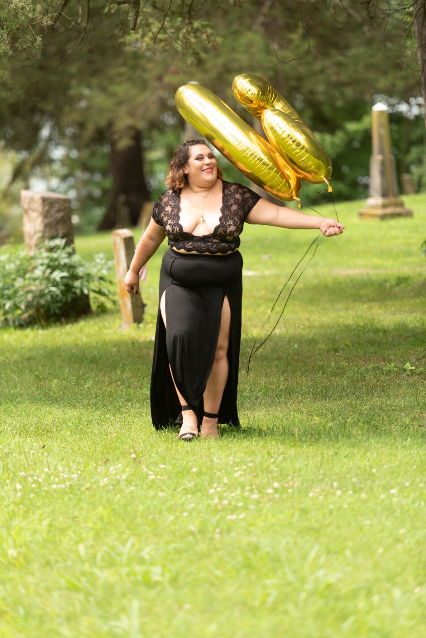  Samantha in black dress walks through cemetery carrying foil letter balloons. 