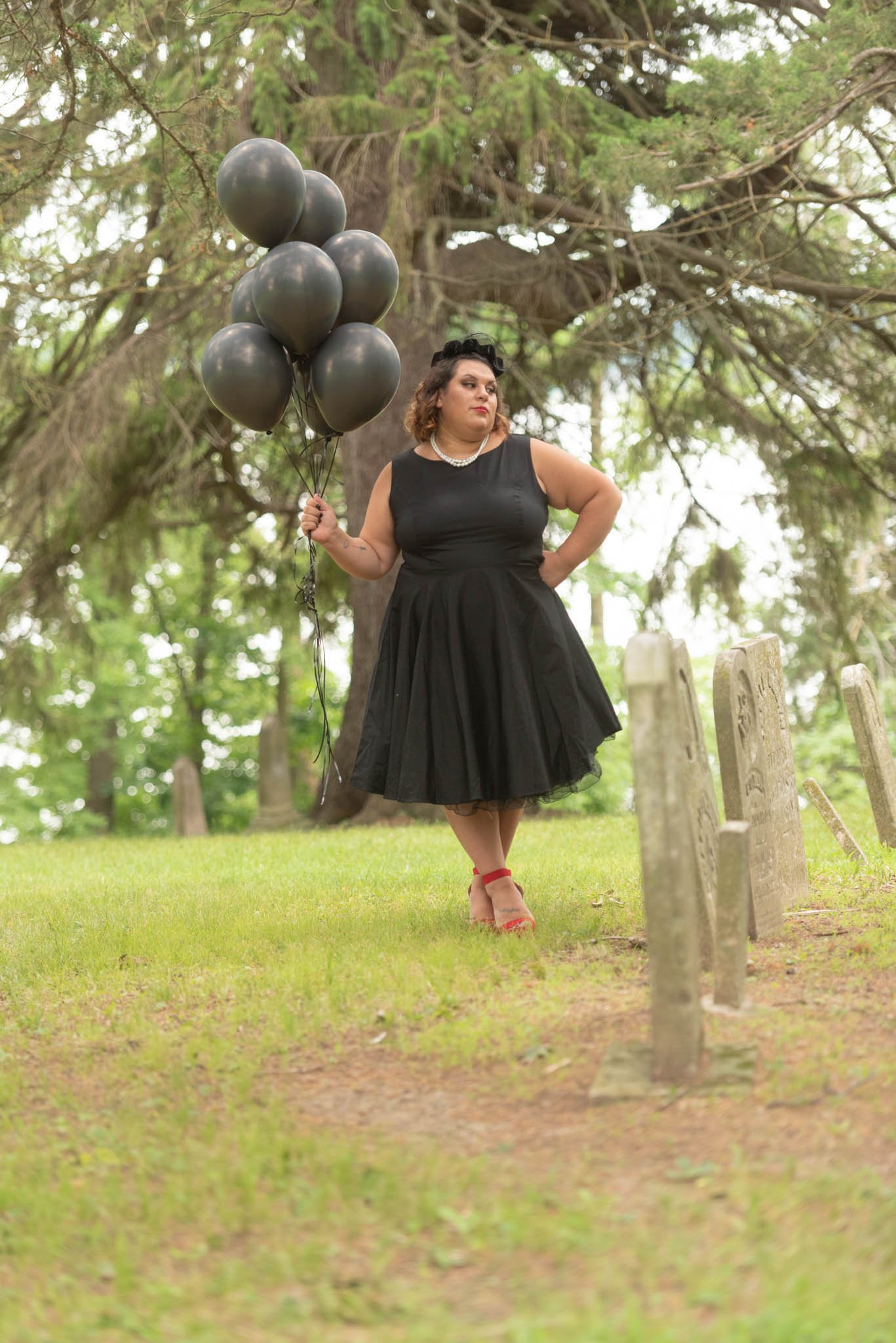  Samantha in black dress and vintage black hat poses in cemetery with black balloons.  