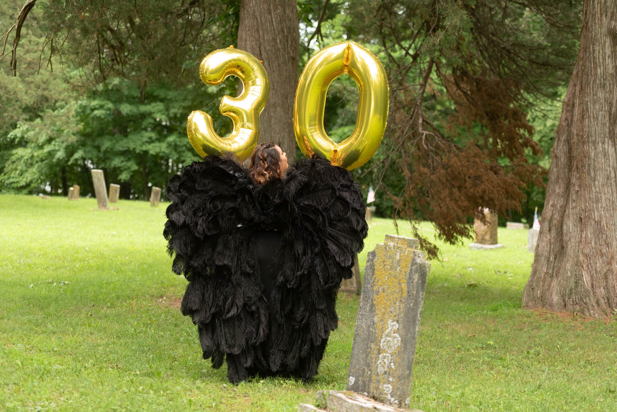  Samantha poses with her back to the camera and displays the number 30 on gold foil balloon letters as she wears black angel wings. 