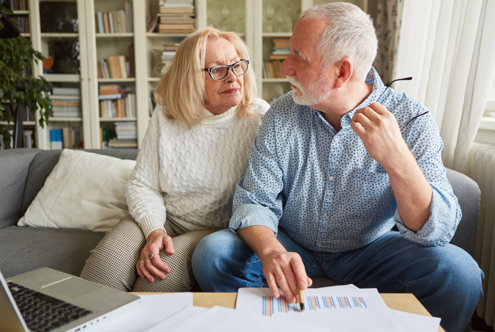 Image showing an older couple sitting on a couch, looking at documents and discussing, possibly related to retirement planning, highlighting the importance of understanding and debunking retirement planning myths for a secure future.