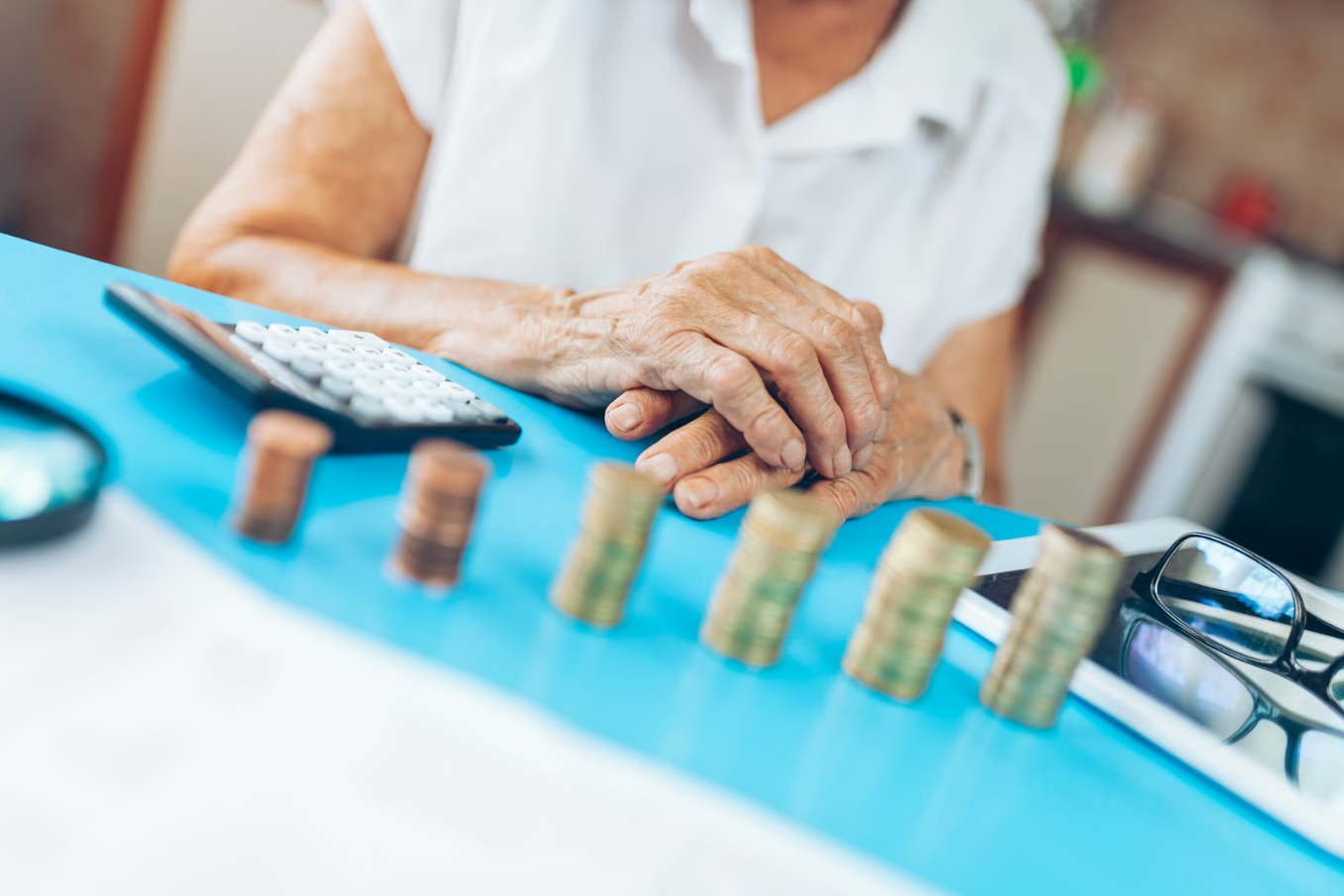 Senior woman planning her retirement savings with a calculator and stacked coins on a table