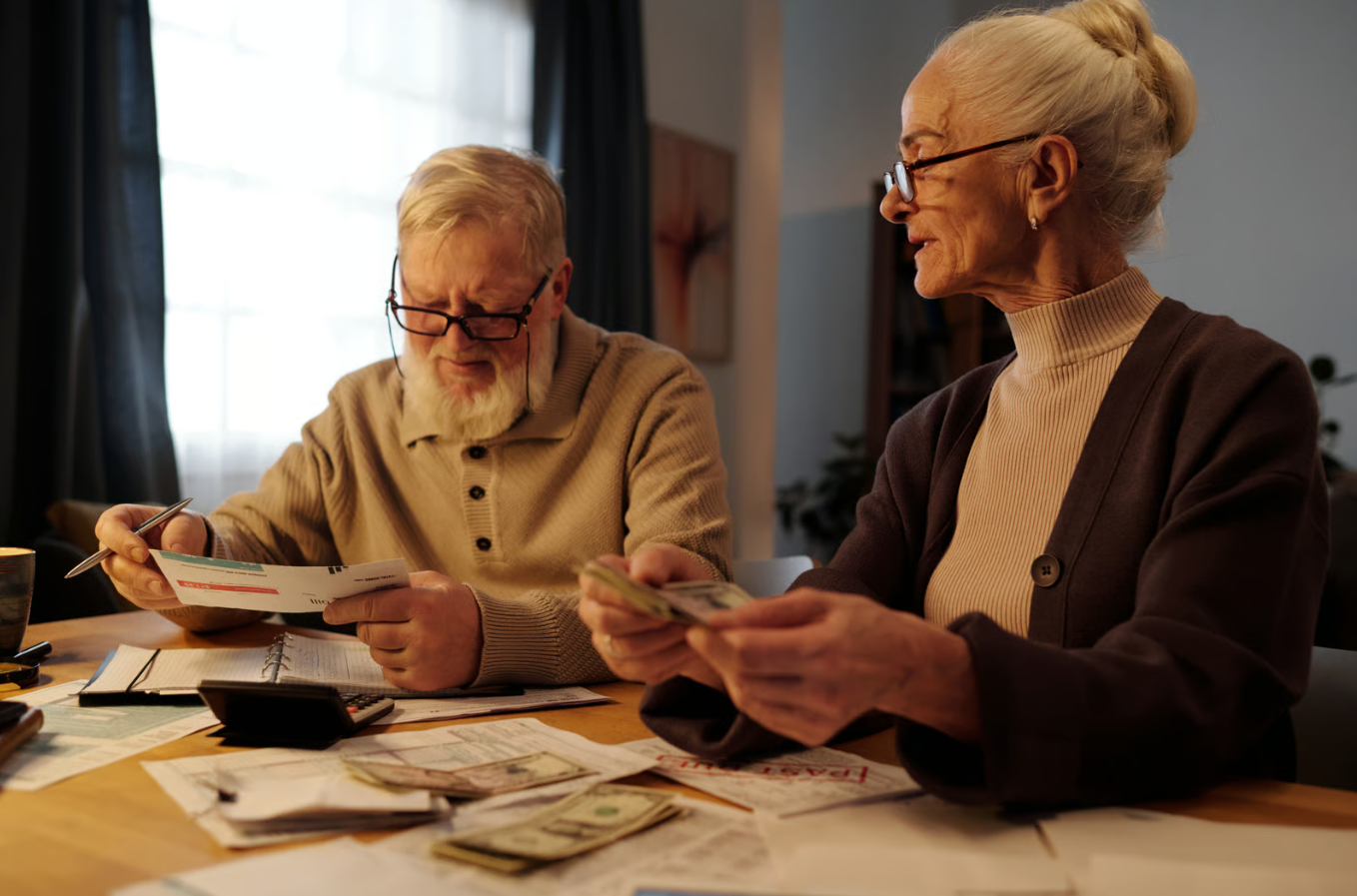 Senior couple reviewing documents and counting cash together while planning their retirement finances at home in Eugene