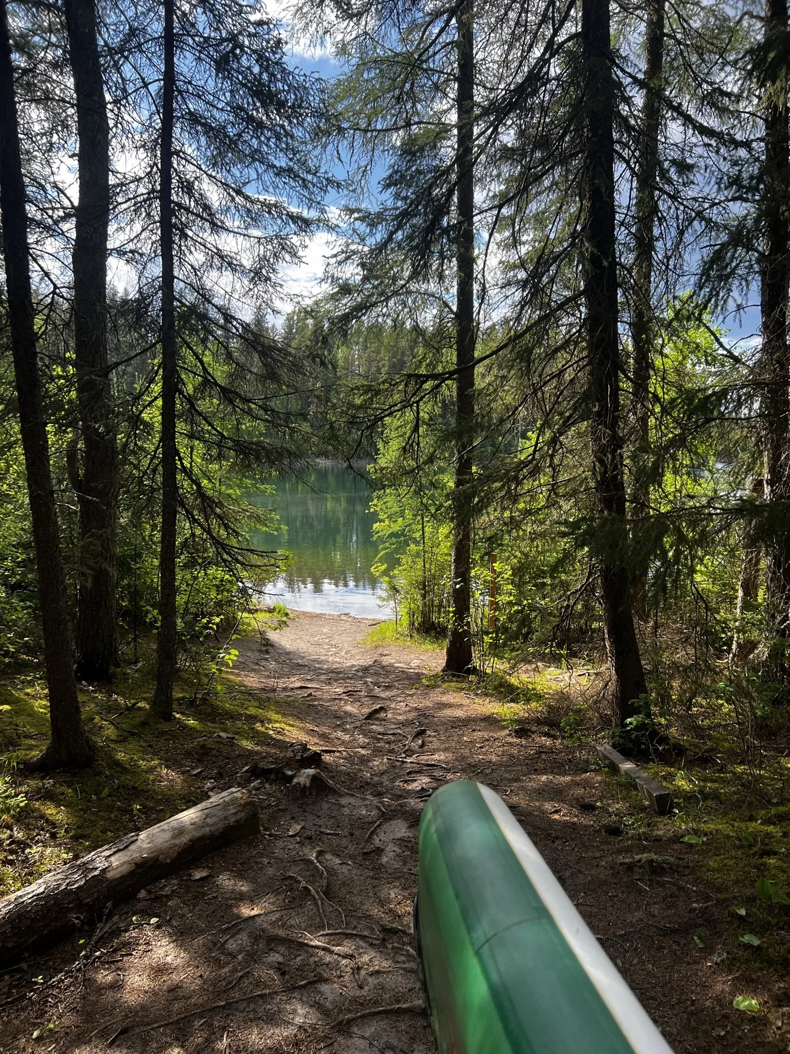 A forest trail leading to a lake, surrounded by trees with a canoe or kayak visible in the foreground.