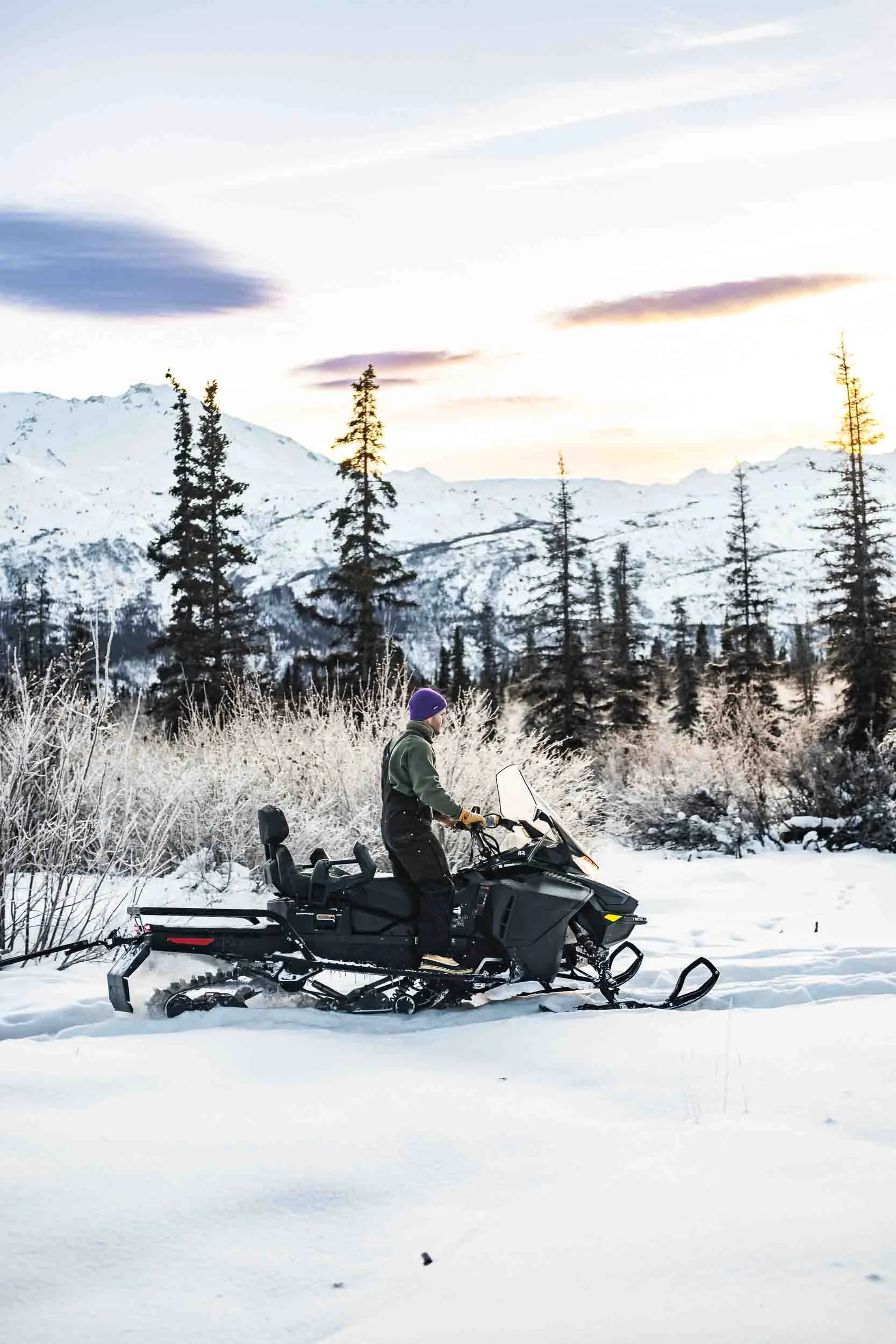 Man riding a snowmobile with towering mountains in the background in Alaska, highlighting adventure photography and video production for outdoor brands.