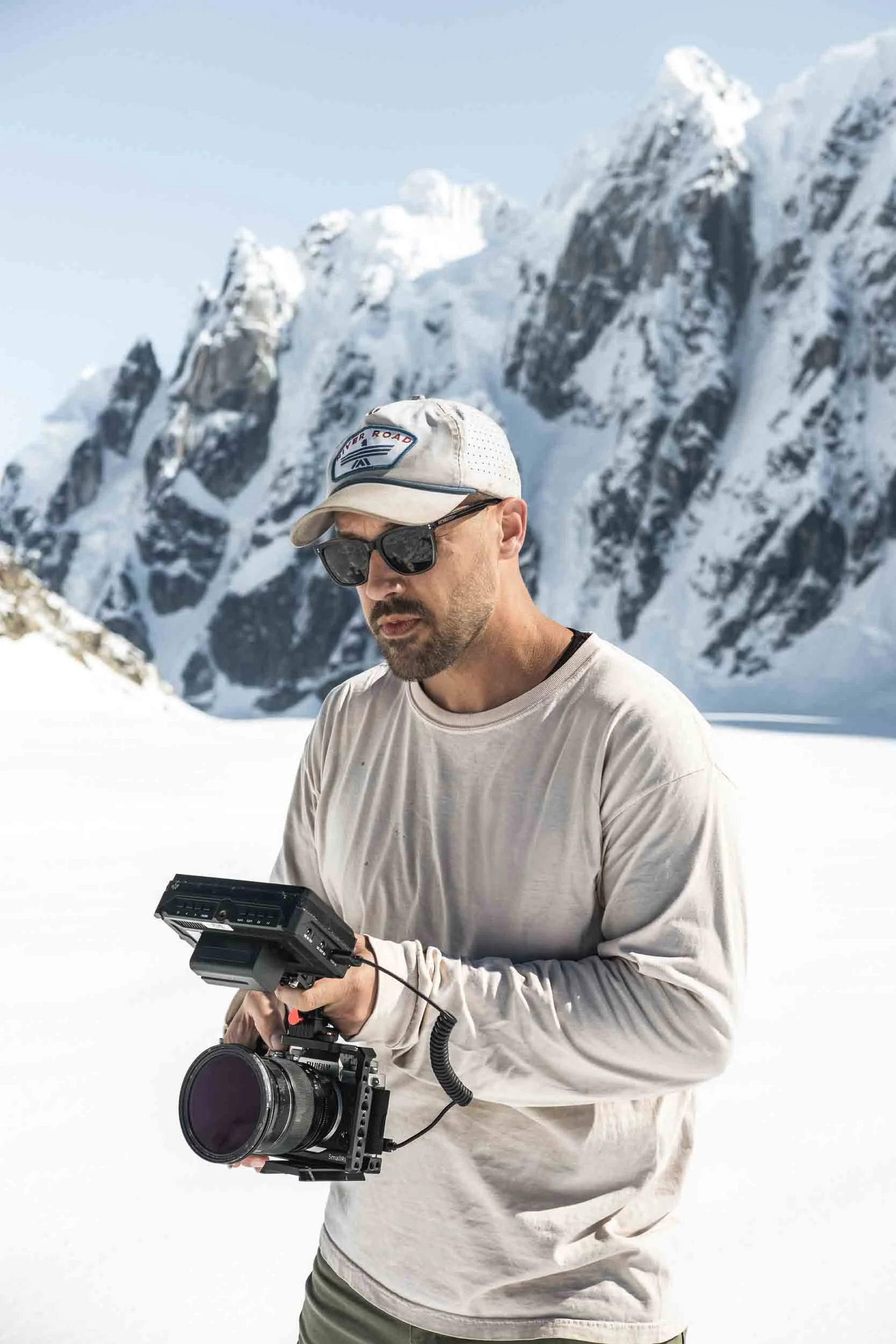 A man holding a camera with snowy mountains in the background in the Alaska range for a commercial photography and film shoot.