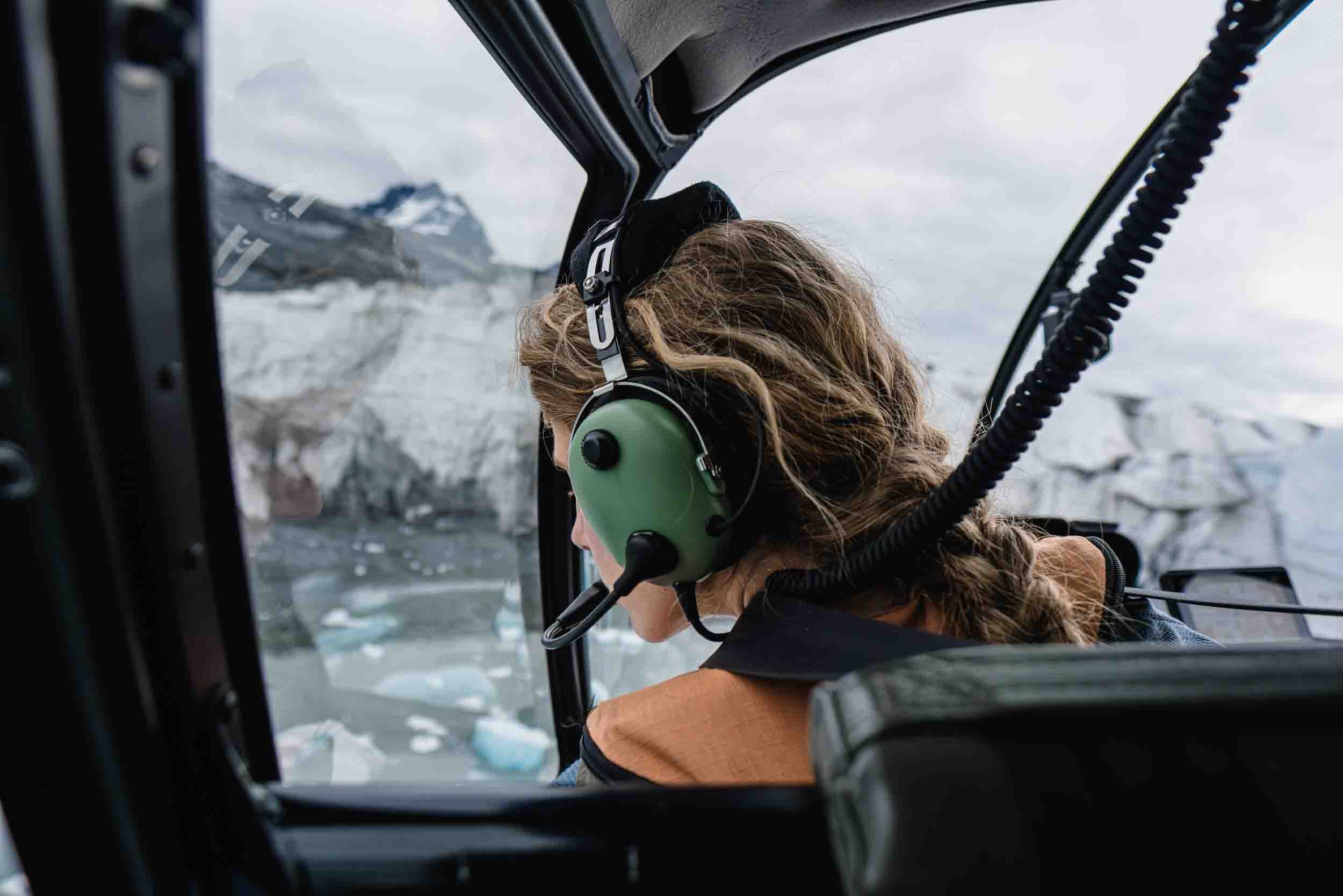 Woman in a helicopter wearing headphones, looking out at Columbia Glacier in Alaska, captured during a cinematic video and photo production shoot.