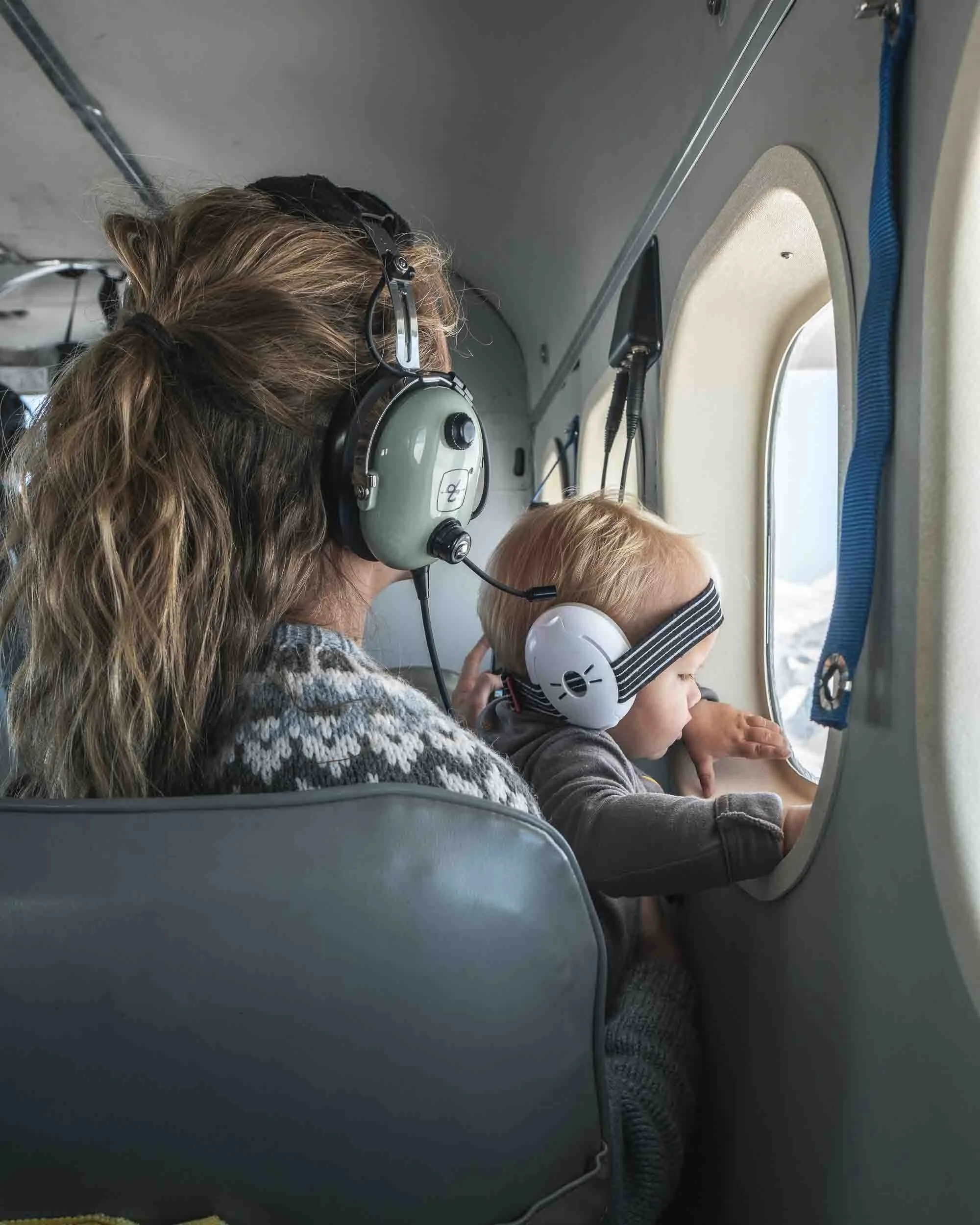 Woman holding a child and looking out the window at the Alaska Range from a de Havilland Otter, en route to a film and photo shoot.