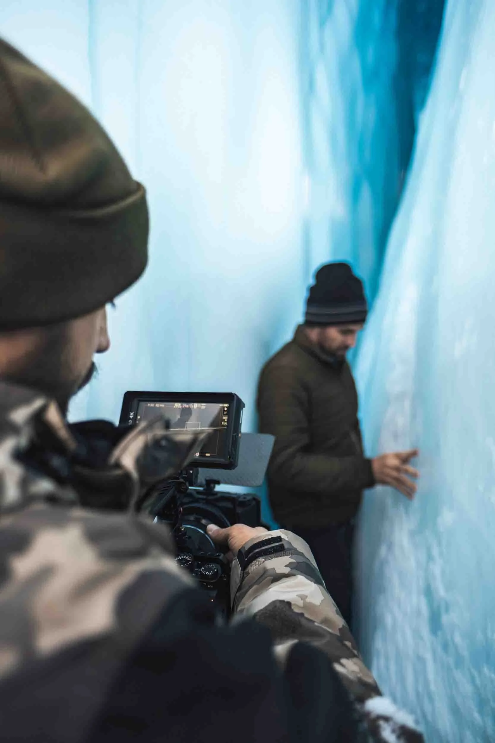 Man holding a camera filming another man in an ice cave on the Matanuska Glacier in Alaska, showcasing adventure-driven video production and commercial photography.