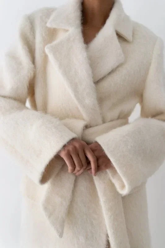 Person wearing a cream-colored coat, with hands clasped in front.